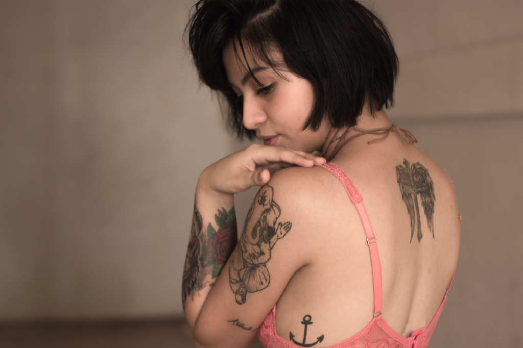 A tattooed woman wearing a bra and looking over her shoulder