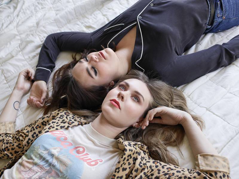The two sisters and member of First Aid Kit are lying down parallel to each other on a soft textile.
