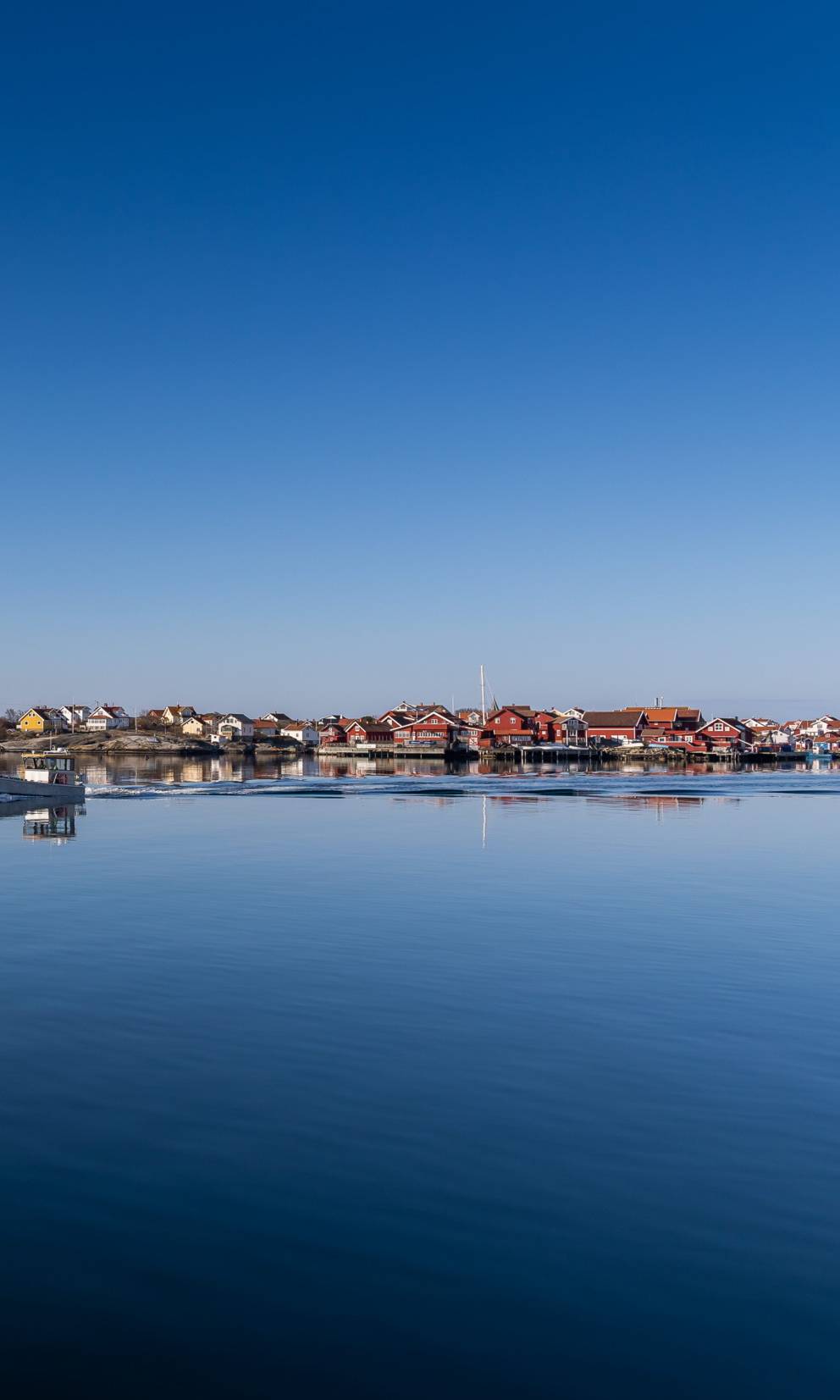 An island in the archipelago with red wooden houses and a white boat in the foreground under clear blue skies.