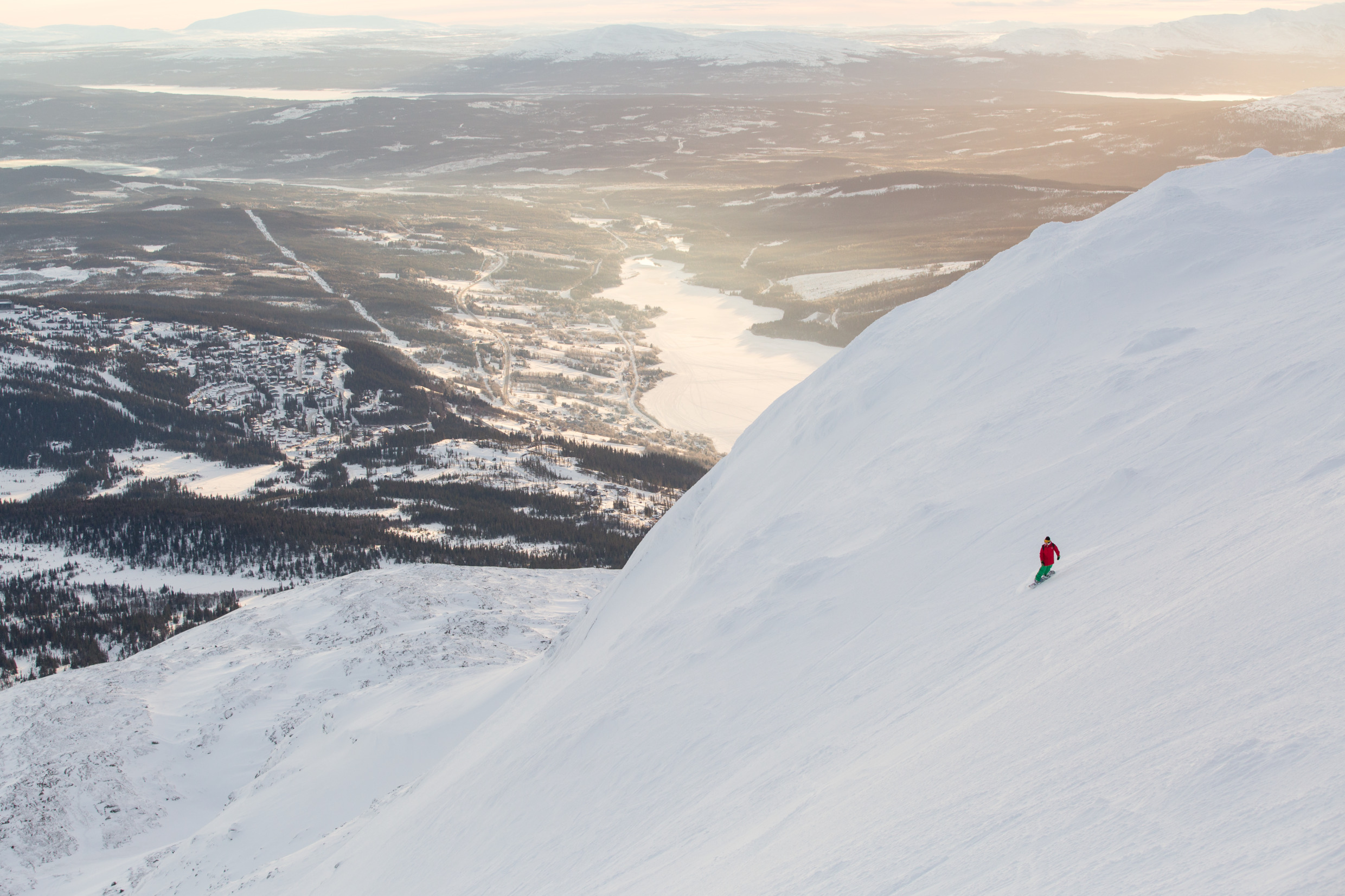 Een schilderachtig uitzicht op de vallei van Åre en een rivier gezien vanaf een van de toppen. Een persoon skiet de helling af.