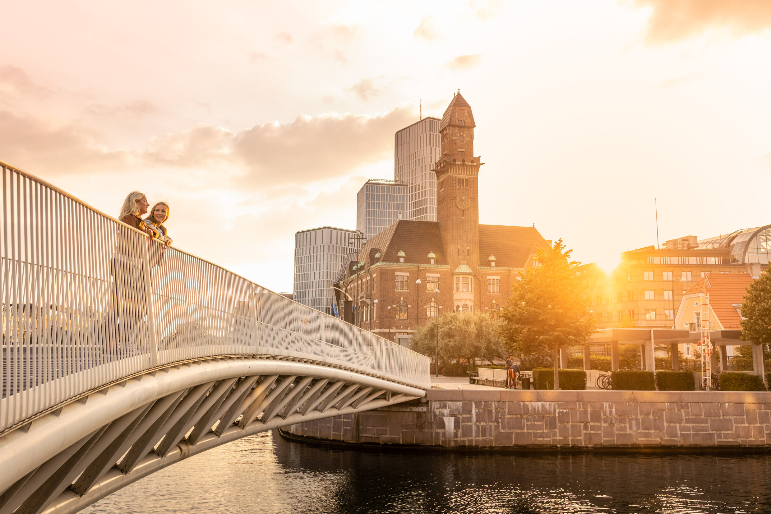 Das Gebäude der WMU in Malmö. Zwei Frauen stehen auf einer Brücke vor dem Gebäude und unterhalten sich.