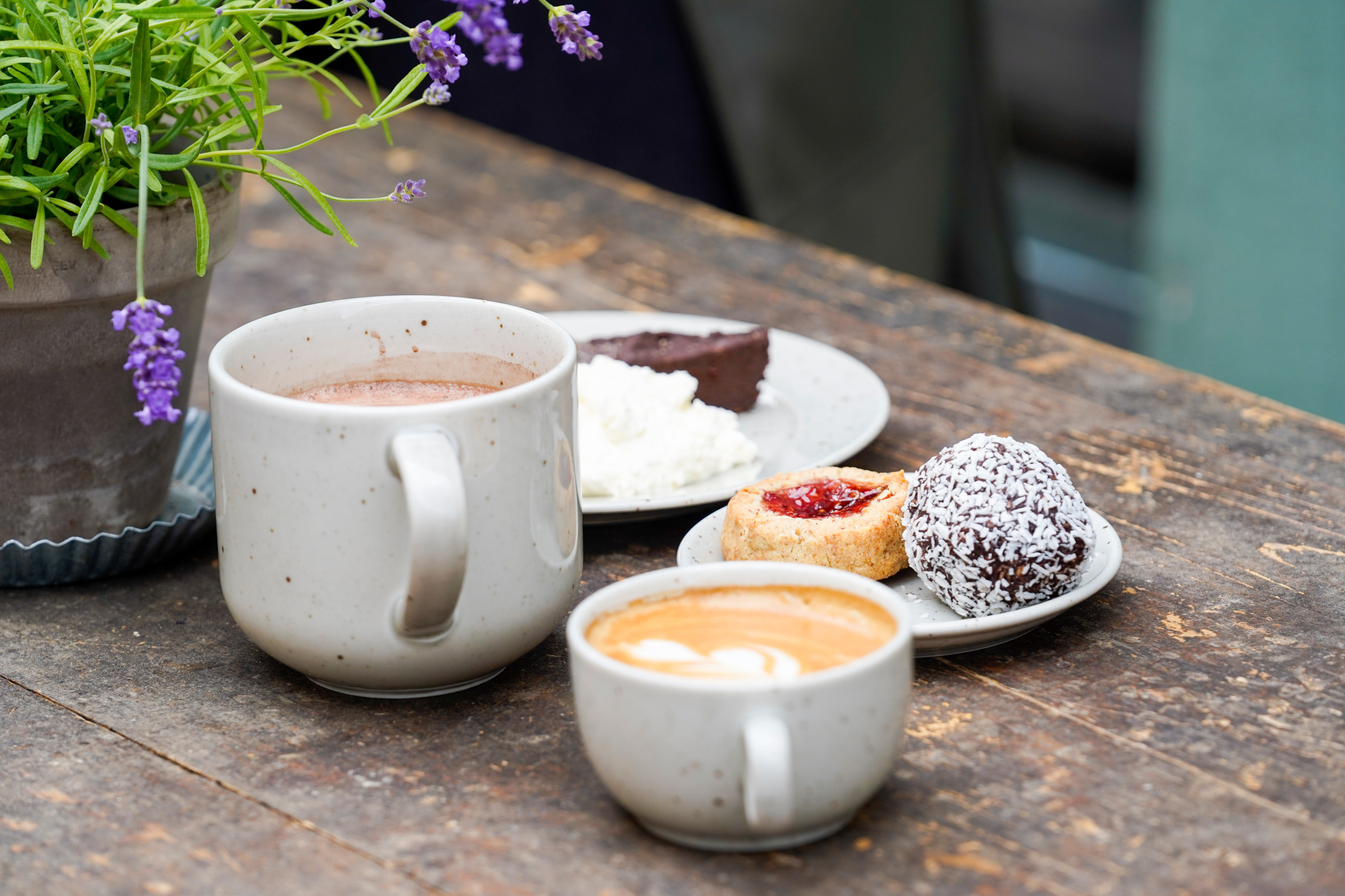 A table with two coffee cups and plates with chocolate cake, chocolate ball and raspberry cave cookie.