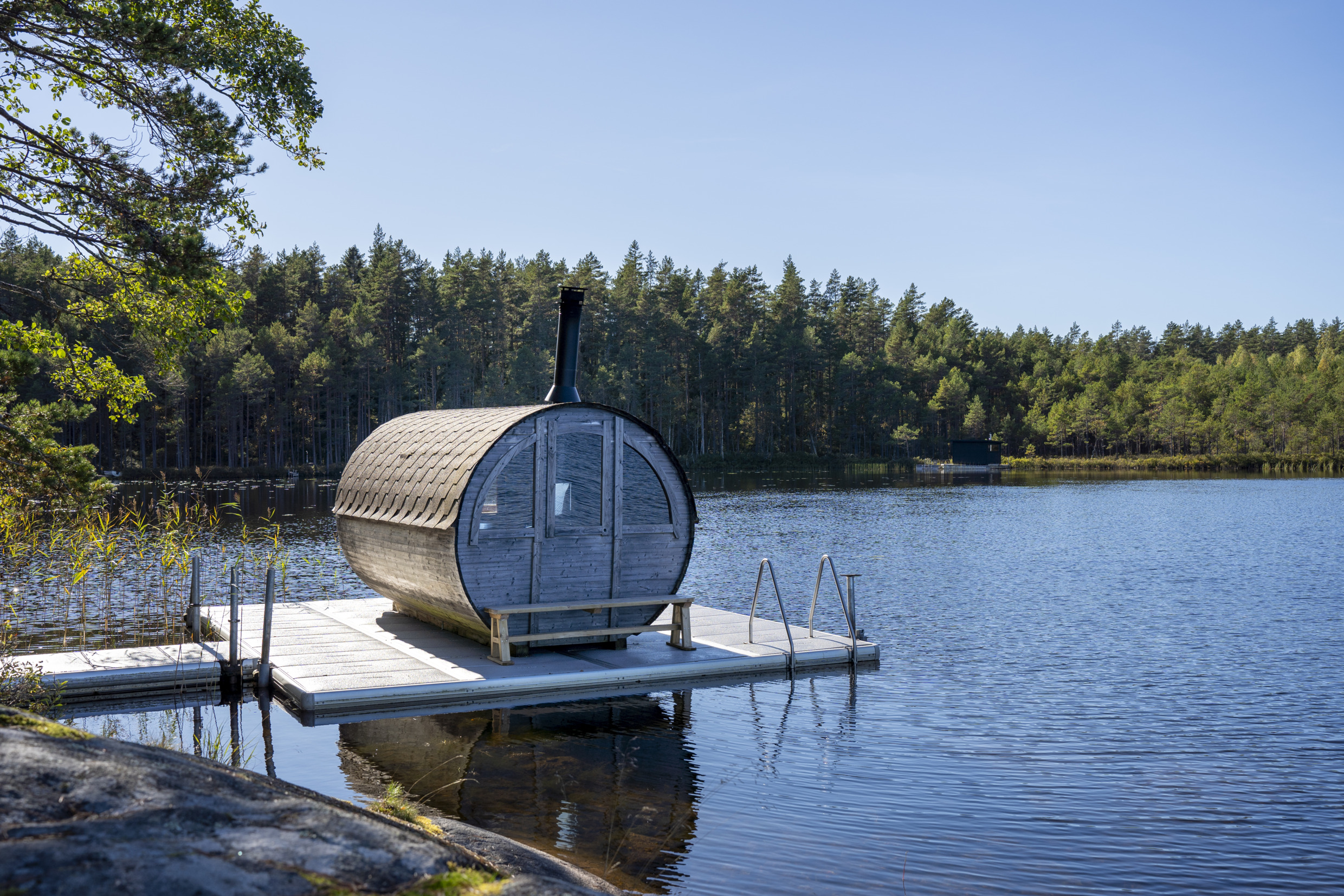 A round sauna floats on the edge of a lake.