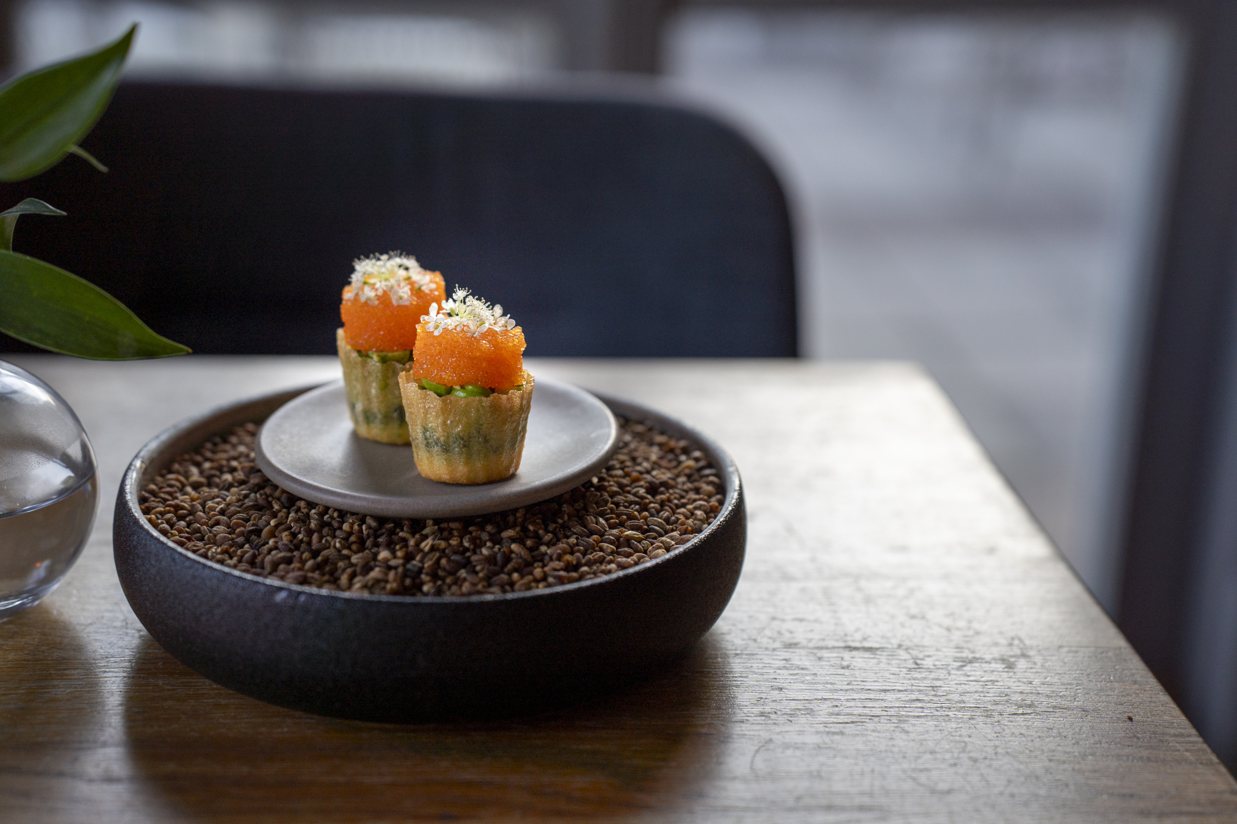 A small canape served in a crisp shell and presented on a plate set inside a bowl filled with coffee beans at Högbo Brukshotell & Spa.