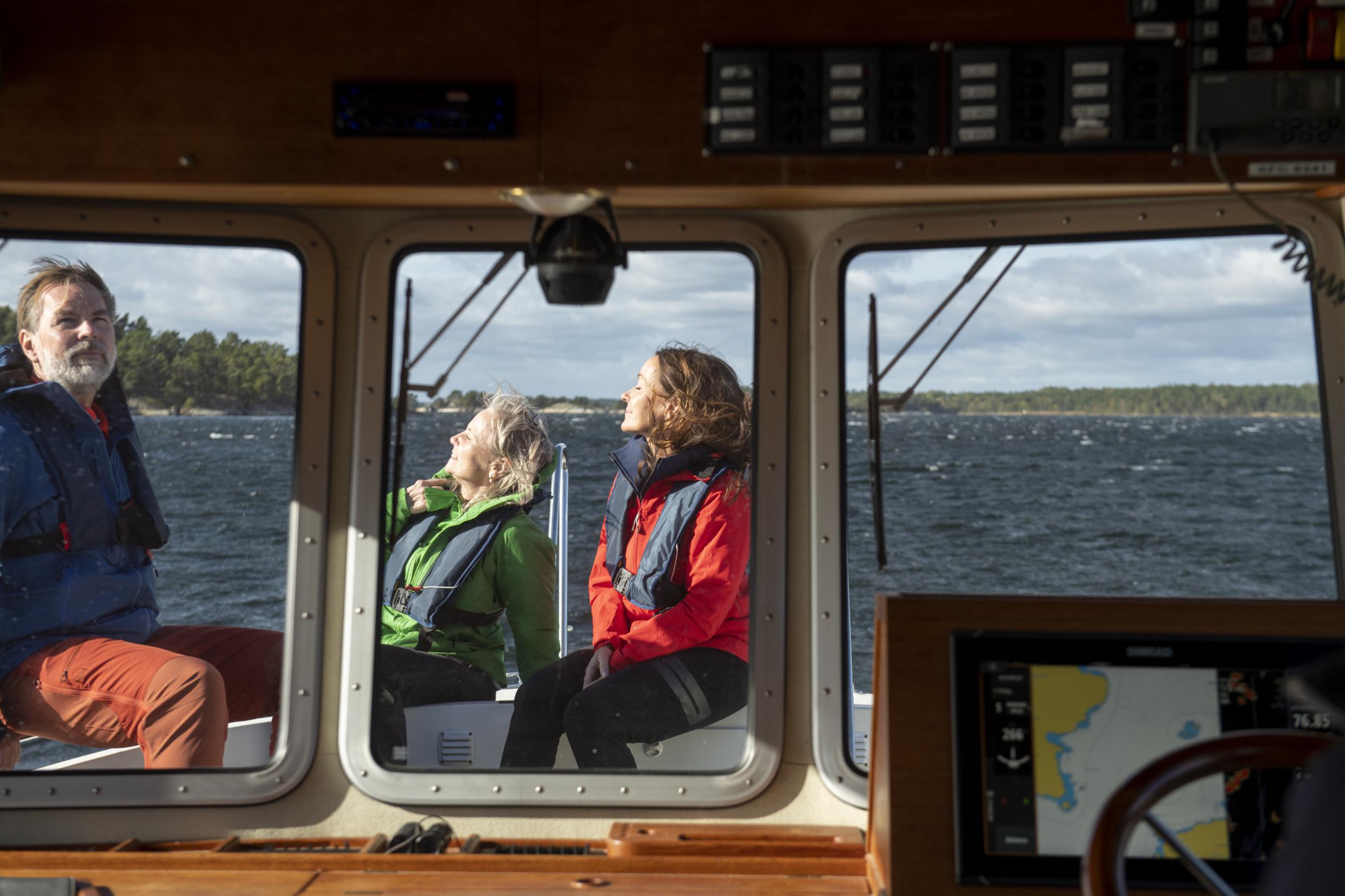 Zwei Frauen und ein Mann sitzen im Freien auf der Vorderseite eines Bootes und genießen die Sonne.