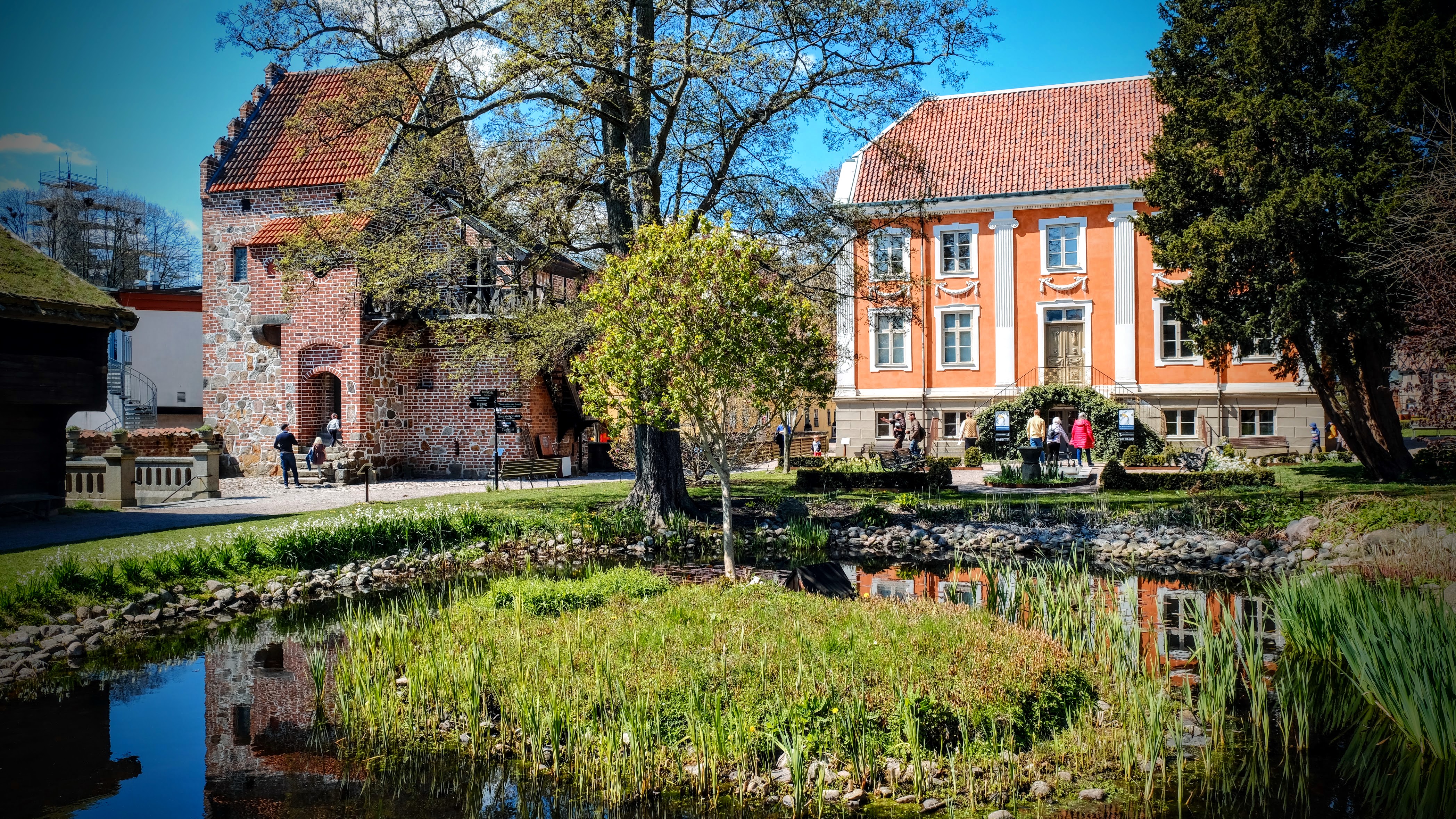 A small pond in front of a large beautiful orange house with white details in the area of the Kulturen Museum.