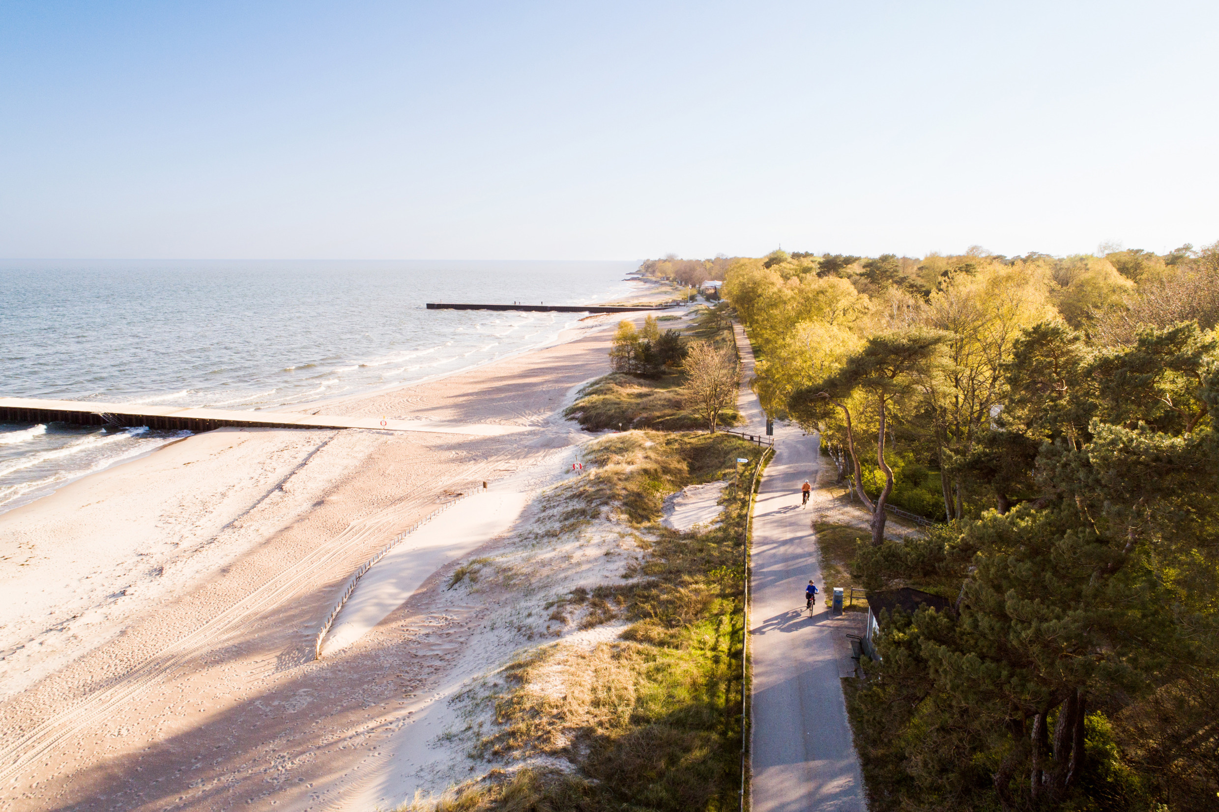 Cycle trail along a white beach with jettys in the ocean. Also lush green trees on the other side of the trail.