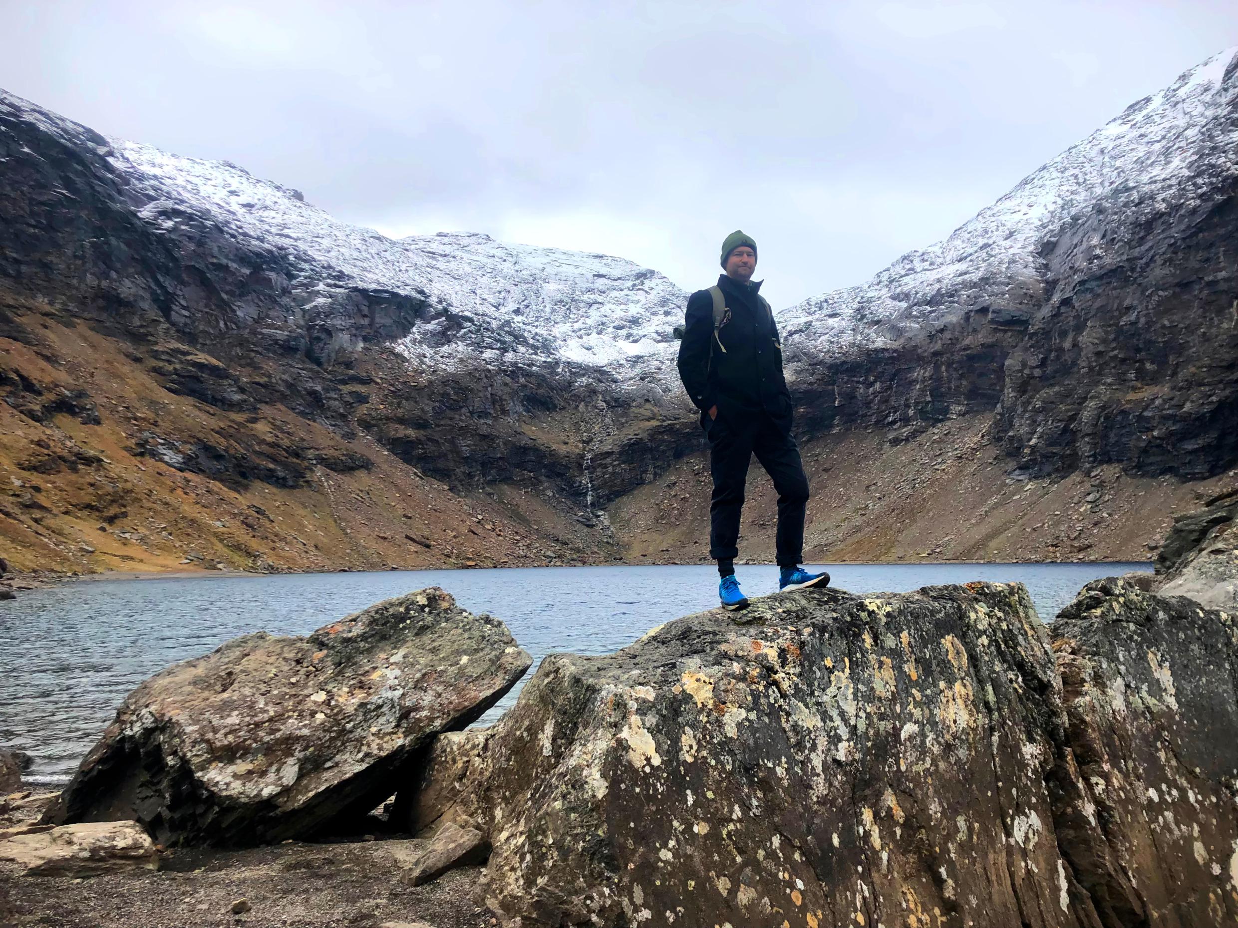 Ein Mann steht auf einem Felsen vor einem von Bergen umgebenen See.