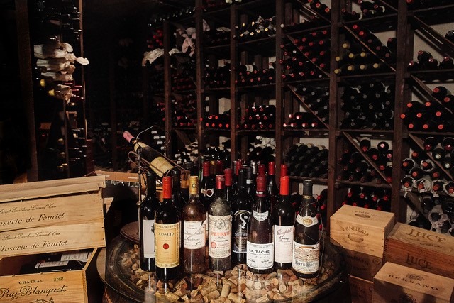 Une cave à vin faiblement éclairée au restaurant 28+ de Göteborg, avec des étagères en bois remplies de bouteilles de vin et des caisses en bois empilées.