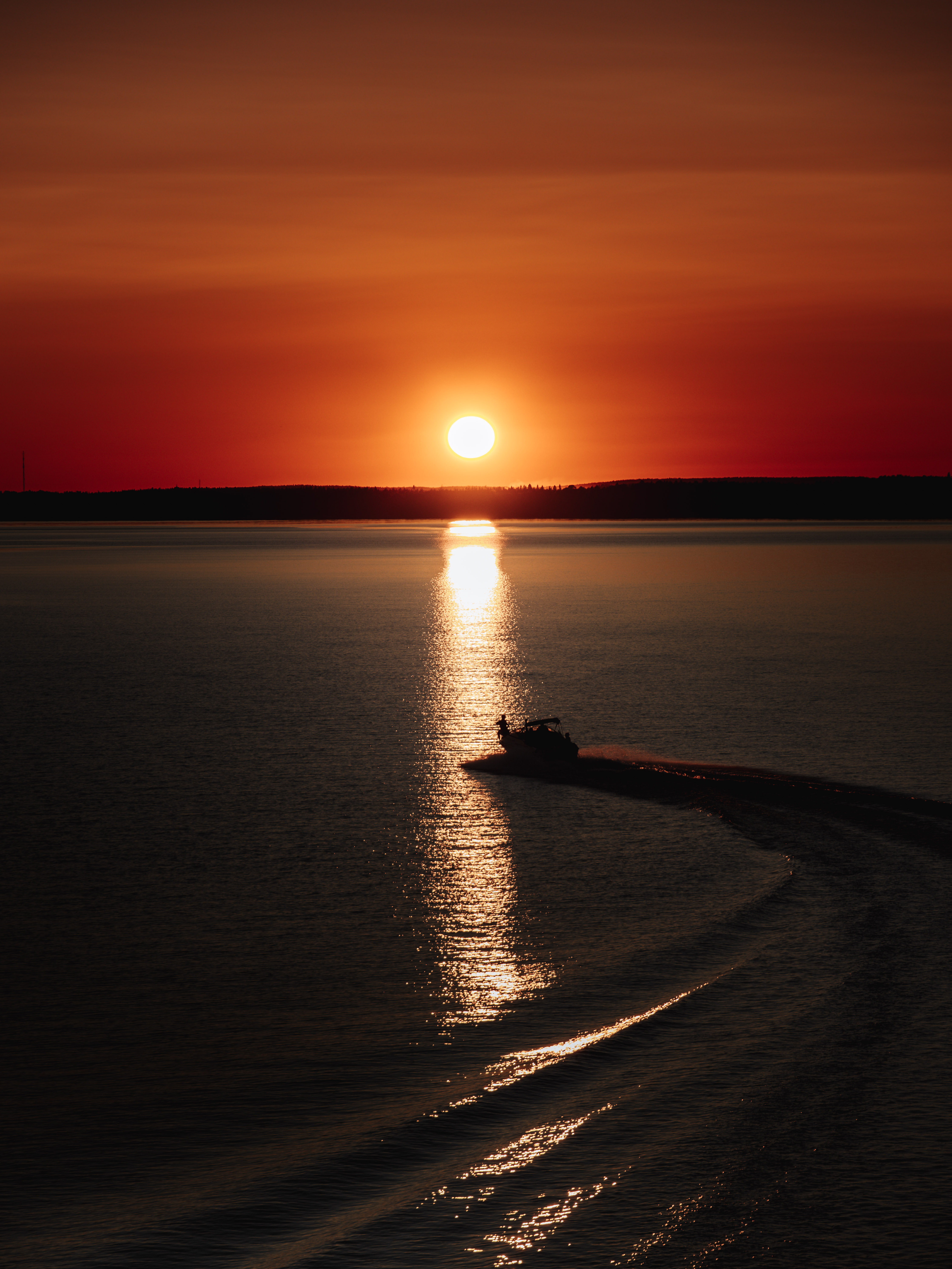 Een boot glijdt over het kalme water bij zonsondergang, terwijl de laagstaande avondzon een gouden schittering werpt in de buurt van Sandön in Luleå.