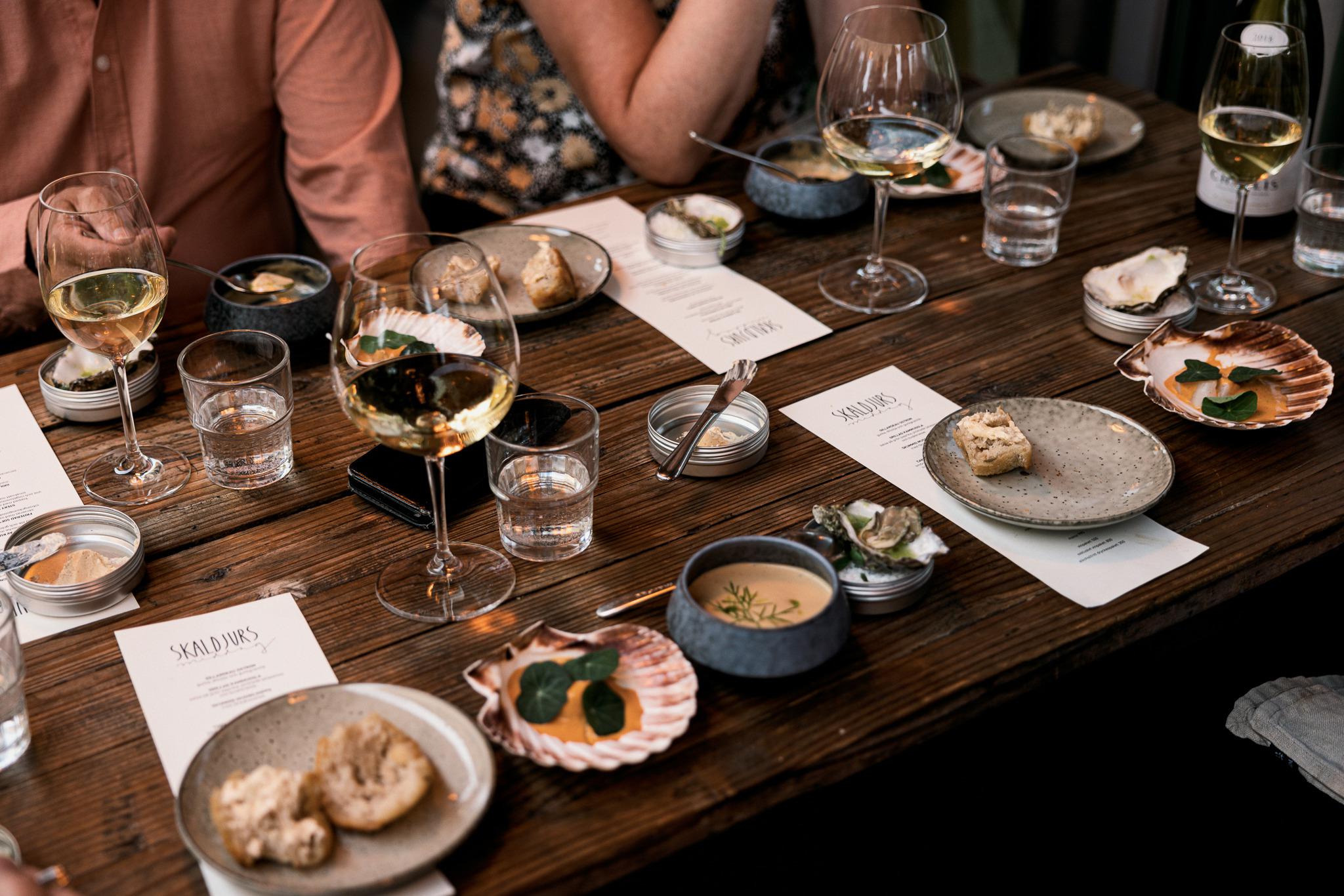 Une table en bois avec des menus, des assiettes avec de la nourriture, des verres à vin blanc et des verres remplis d'eau.