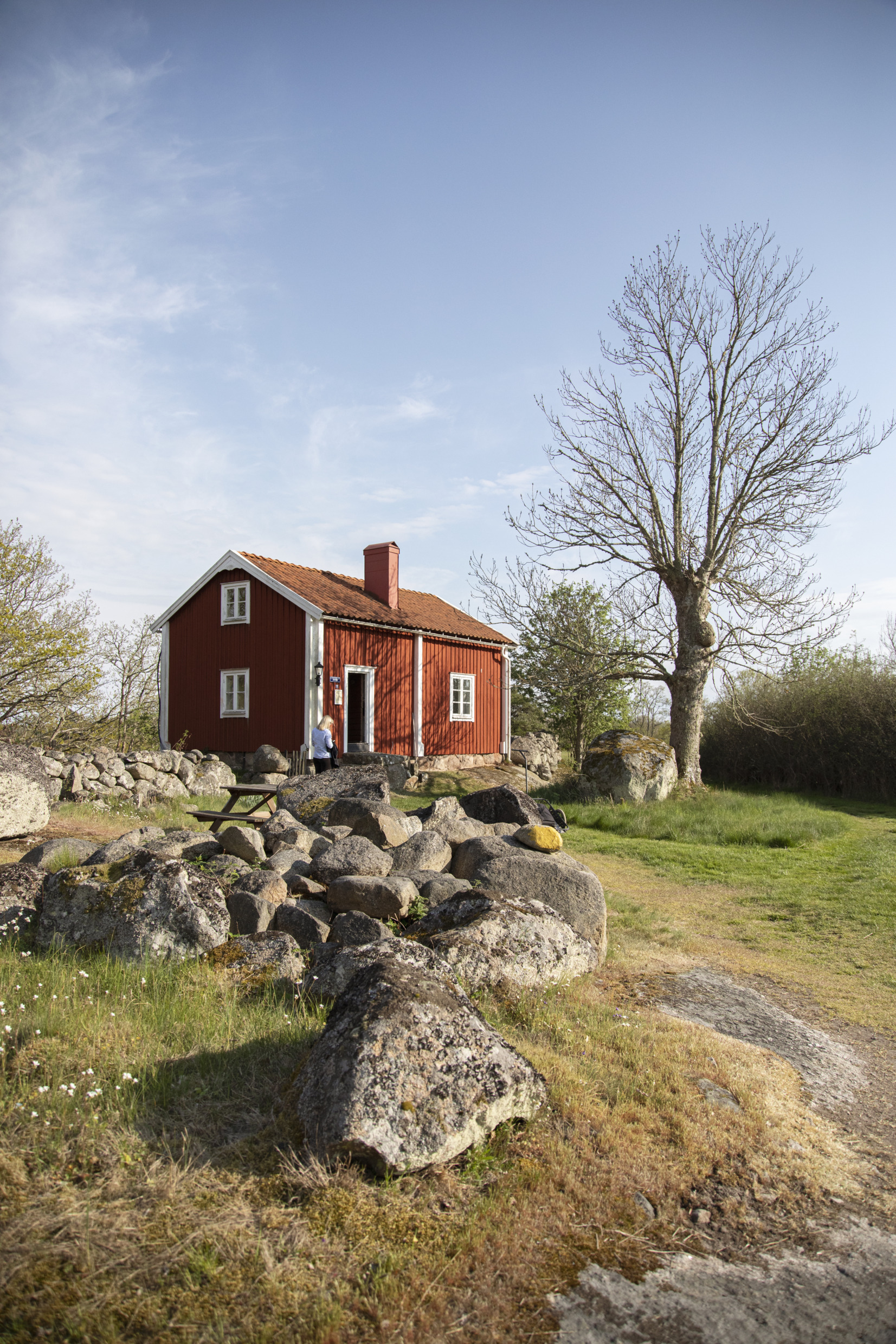A person walks in front of a traditional red cottage with white trims.