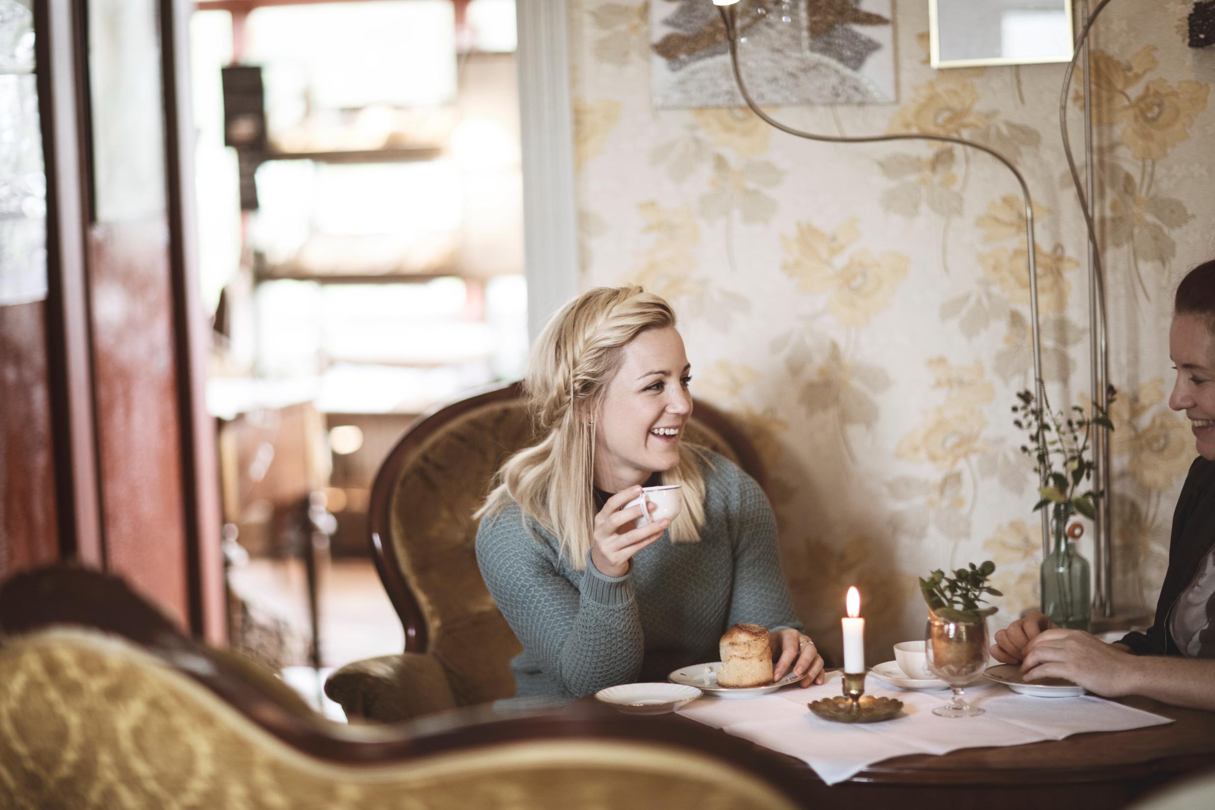 Twee lachende vrouwen eten gebak en drinken warme dranken in een café.