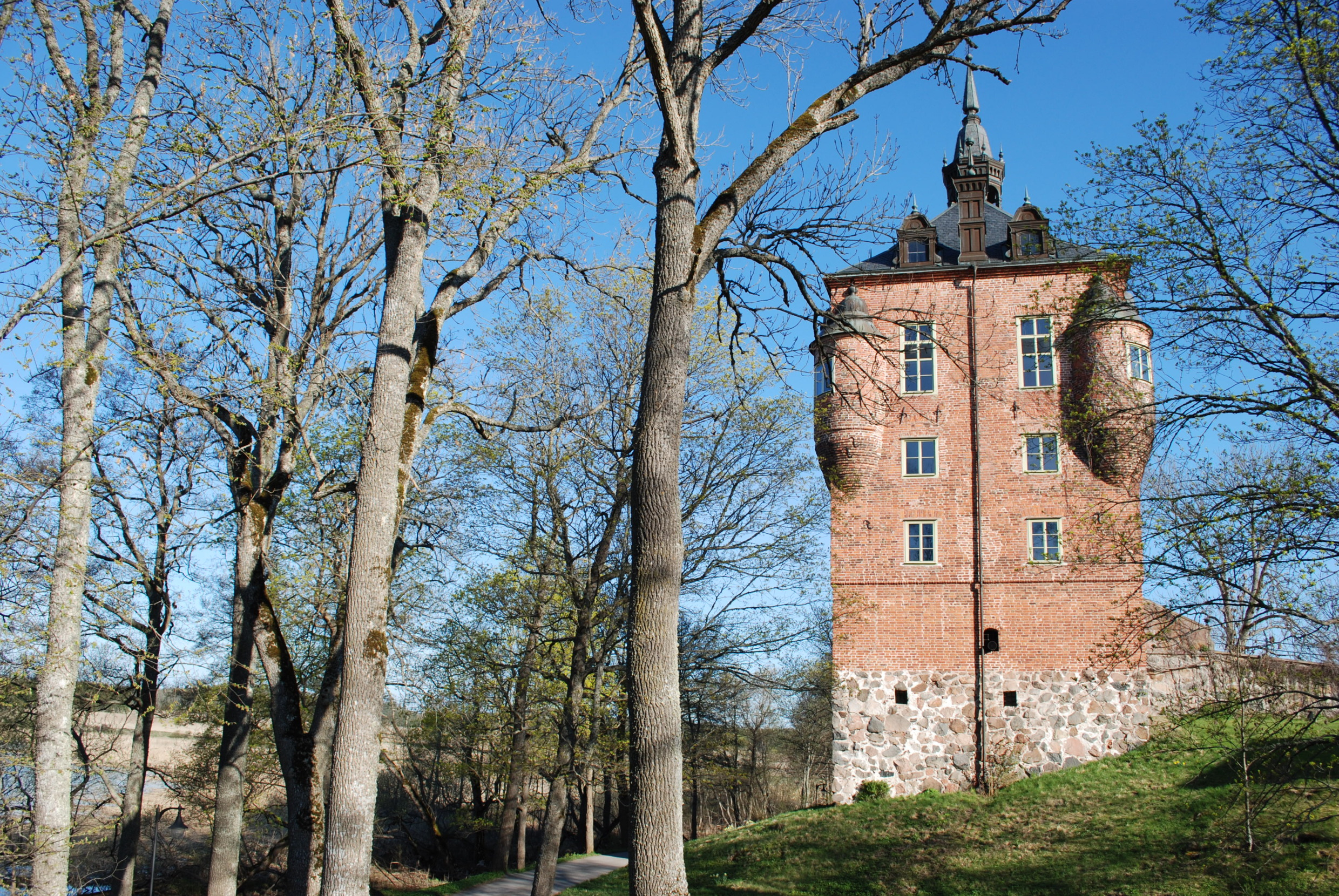 De rode bakstenen toren van Wik Castle, omringd door bomen en een blauwe lucht in de lente, Uppsala.