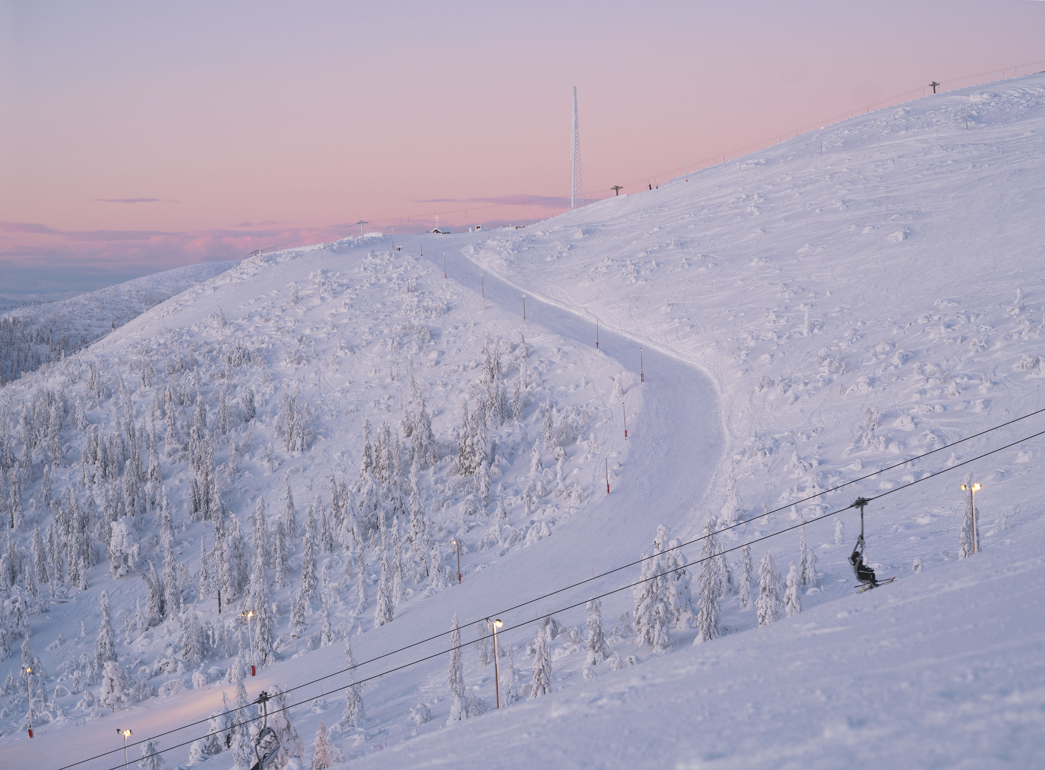 Ski slope and trees covered in snow during evening skiing in Björnrike, with soft pink light on the horizon.