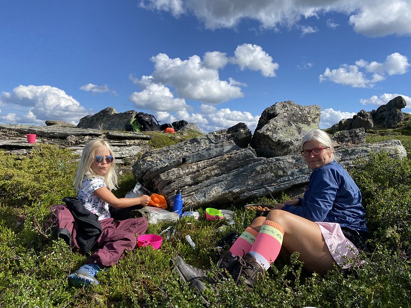 An adult and a child sitting on the ground among rocky terrain, enjoying a lunch break during a hike to Helags glacier in Ljungdalsfjällen.