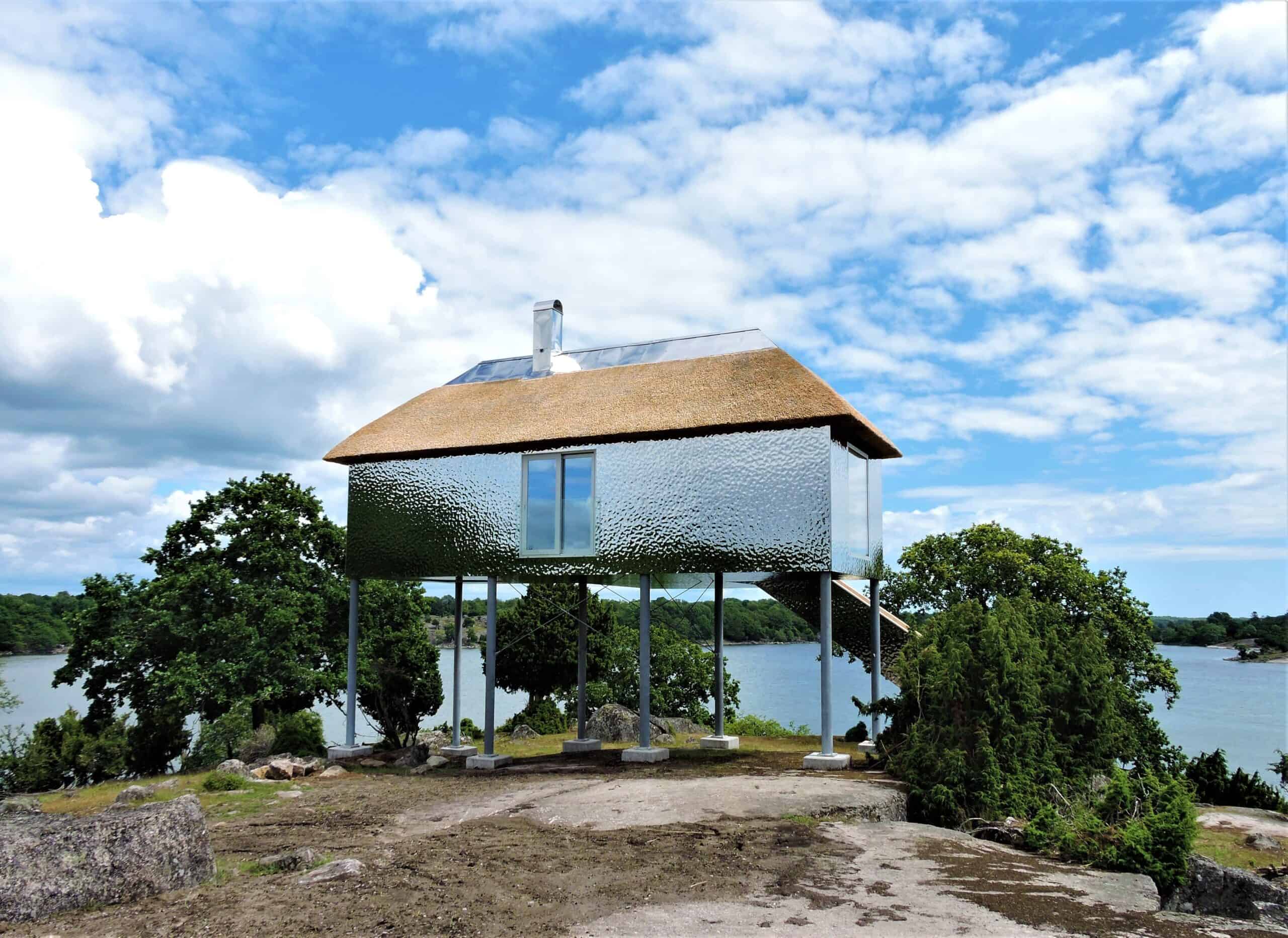 Synvillan in Eriksberg, een met zilver bekleed gebouw met een rieten dak, hoog op palen gebouwd met uitzicht op het water en de omliggende bossen.
