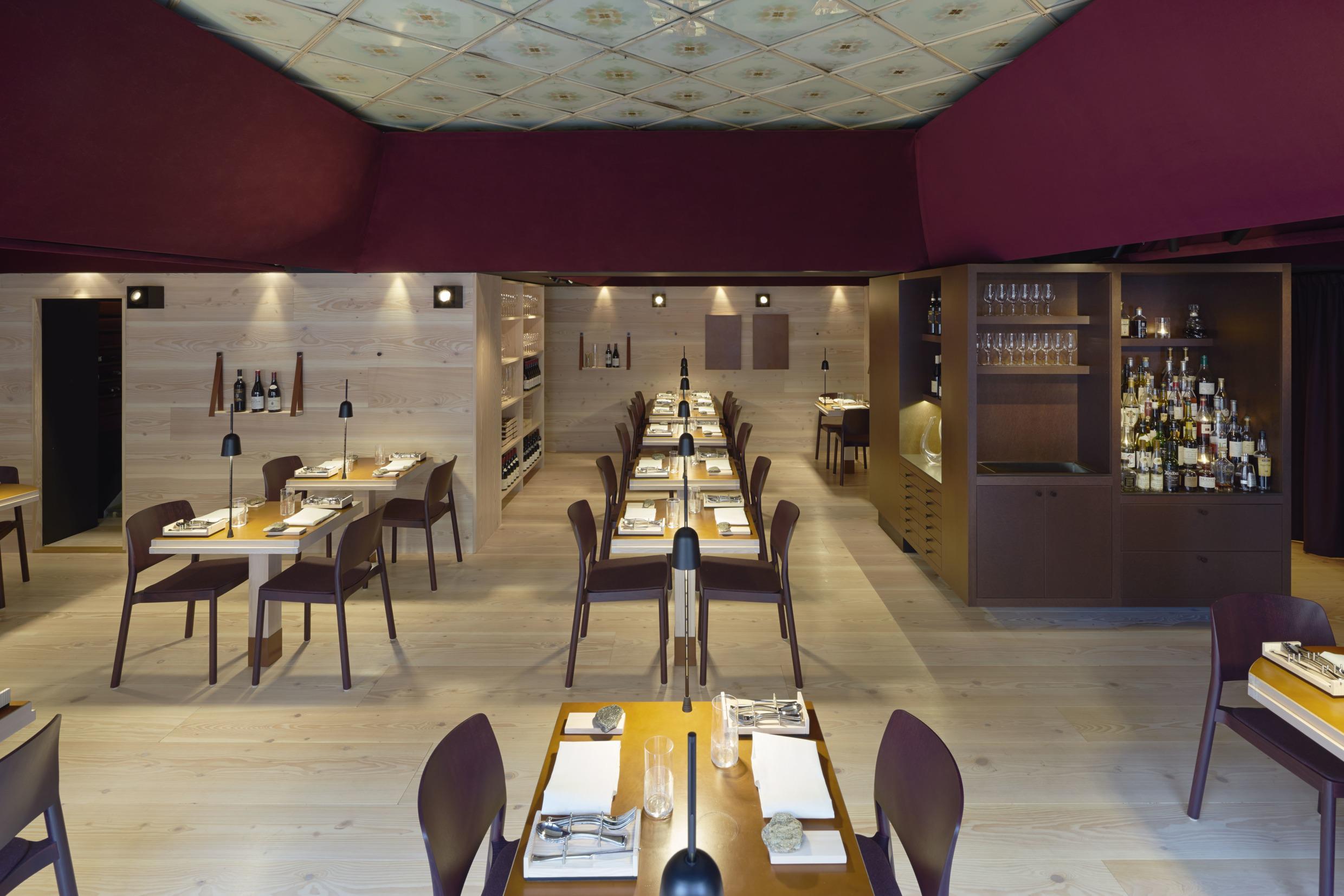 Das Innere des Restaurants Koka mit Holzwänden und dunkelroter Decke. Mehrere gedeckte Tische und ein Barregal im Raum.