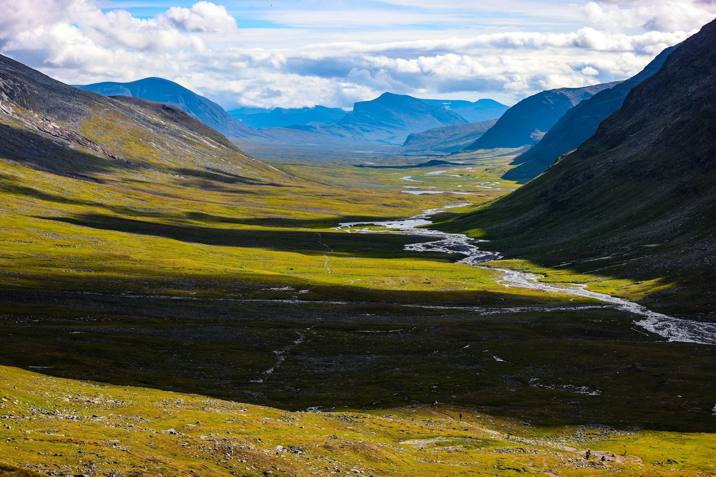 Majestic landscape view of Kungsleden. River surrounded by mountains, cloudy sky and sunshine.