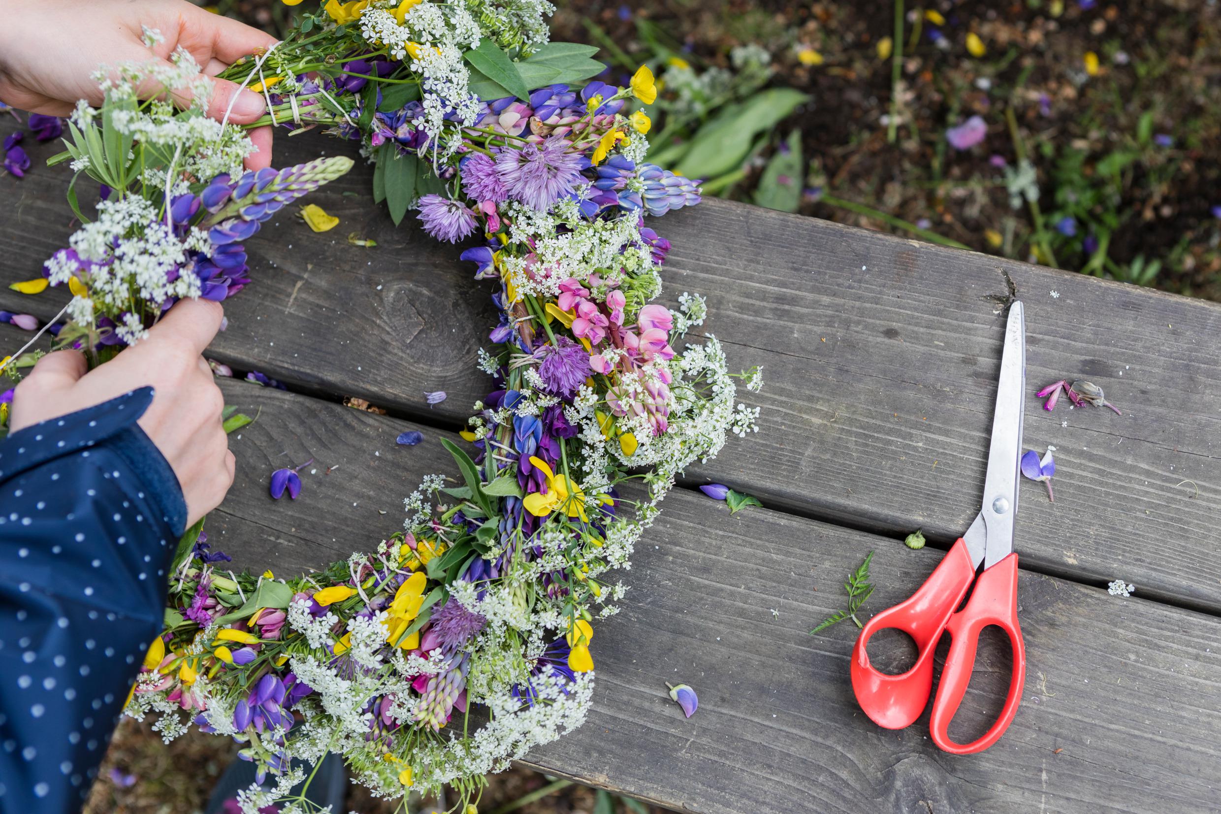 Iemand maakt een bloemenkroon. Er ligt een schaar op een houten tafel.