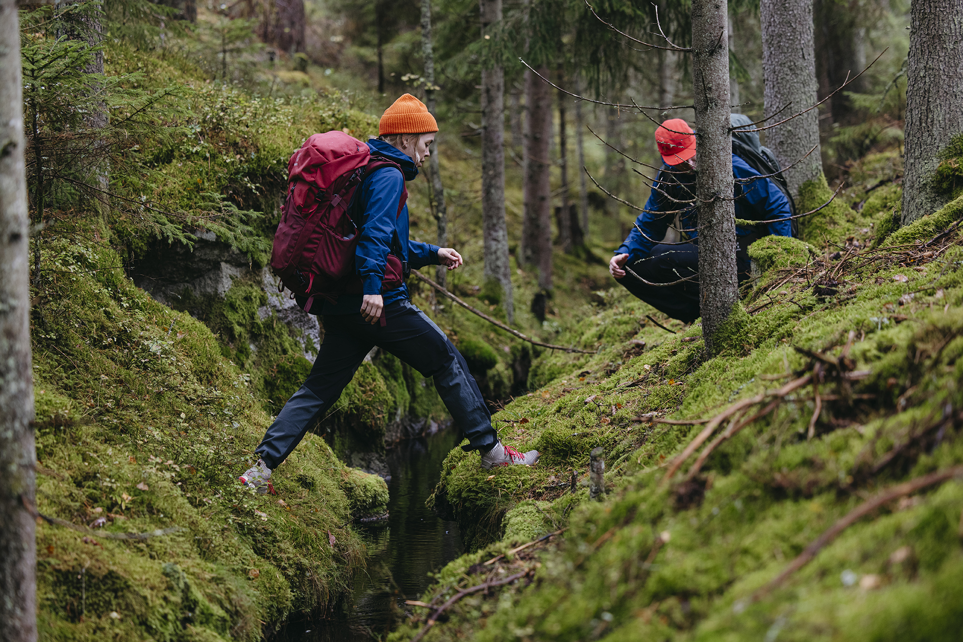 Zwei Wanderer überqueren einen kleinen Bach in einem Wald mit moosbedecktem Boden entlang des Emigrant Trail.