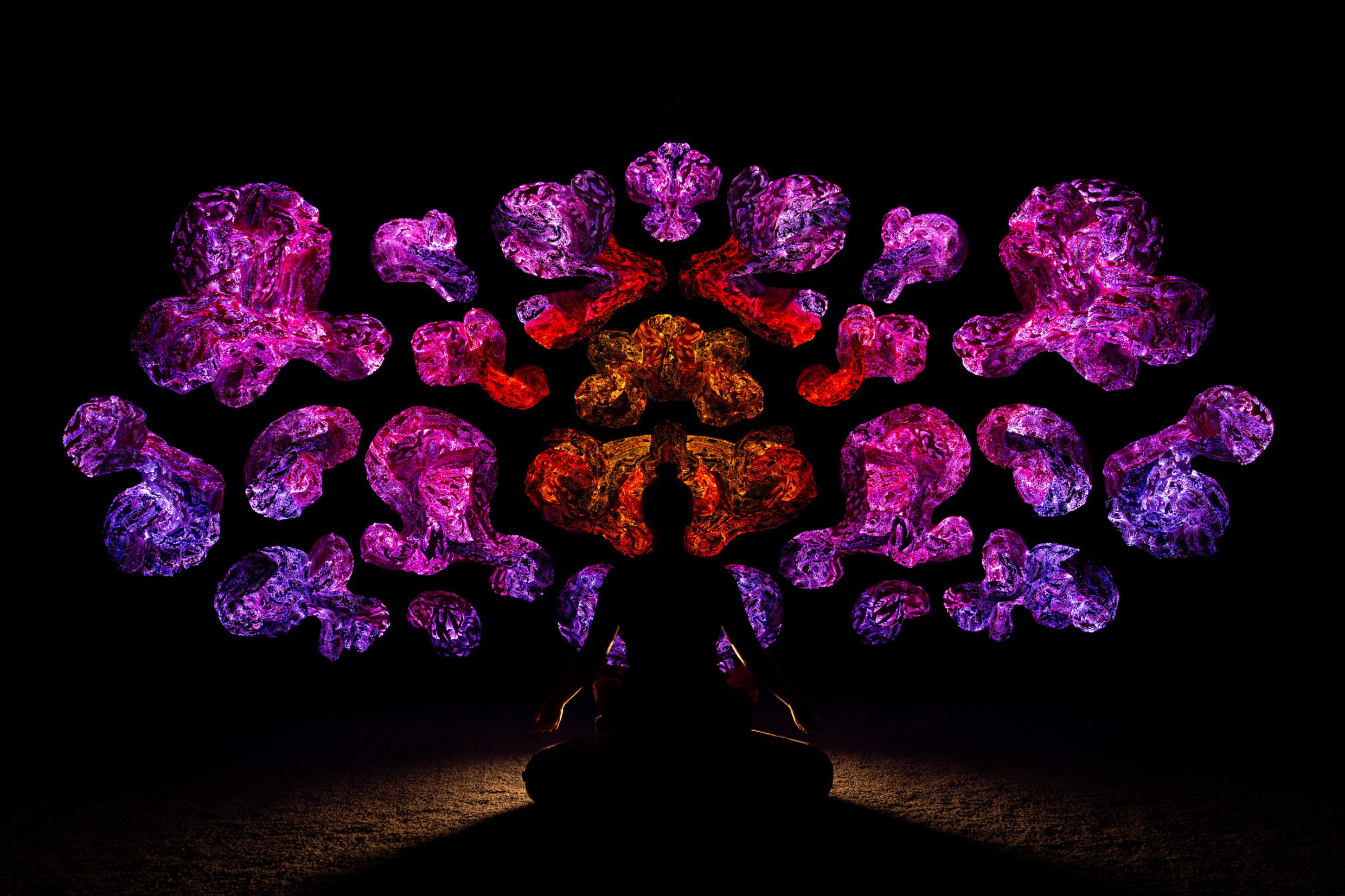 Silhouette d'une personne assise en méditation devant des sculptures textiles illuminées à Andetag, une installation artistique contemplative à Stockholm.