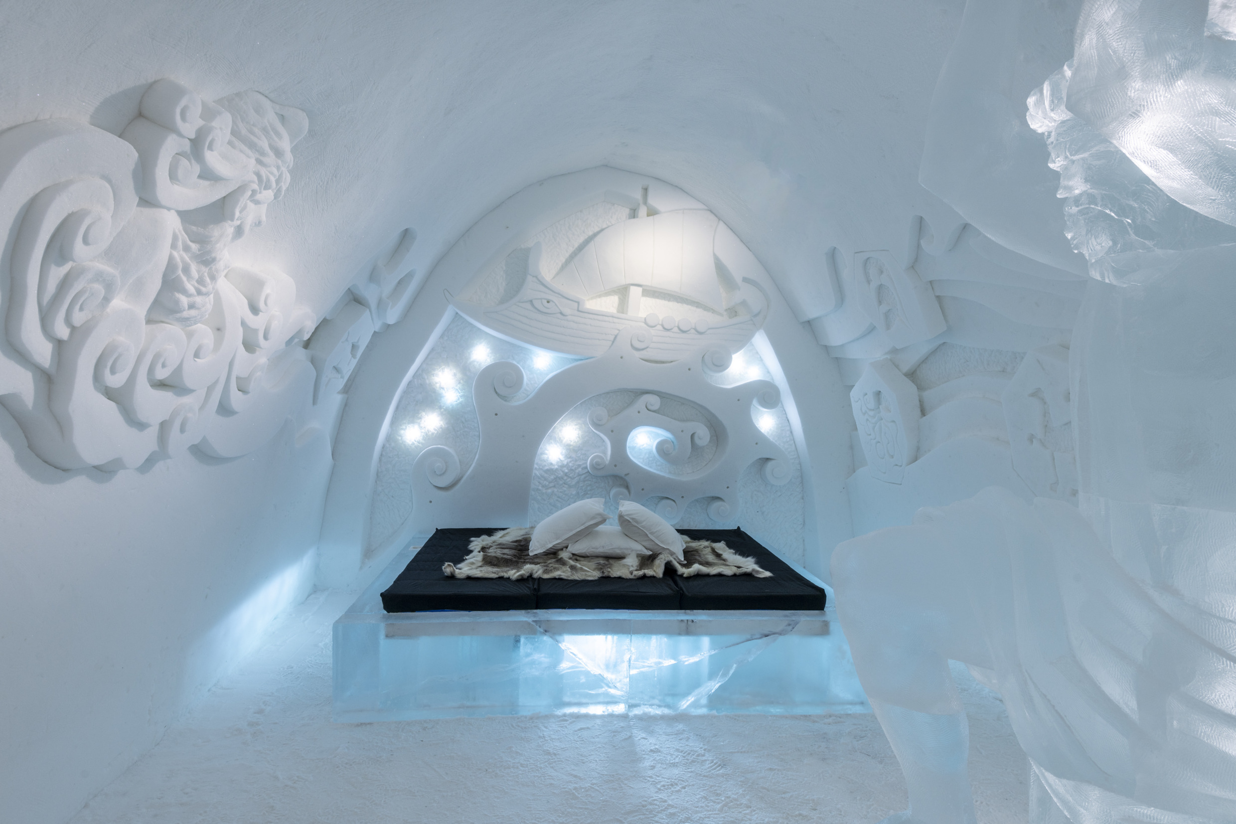 Suite at the Icehotel in Jukkasjärvi featuring a bed made of ice covered with reindeer hides. Ice art carved into the walls.