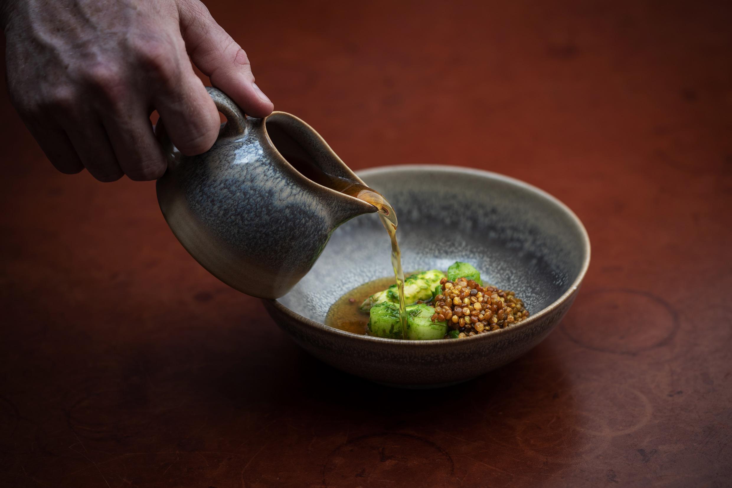 Jemand gießt eine klare Flüssigkeit aus einem Saucenspiegel über das Gemüse in einer kleinen Schlüssel..