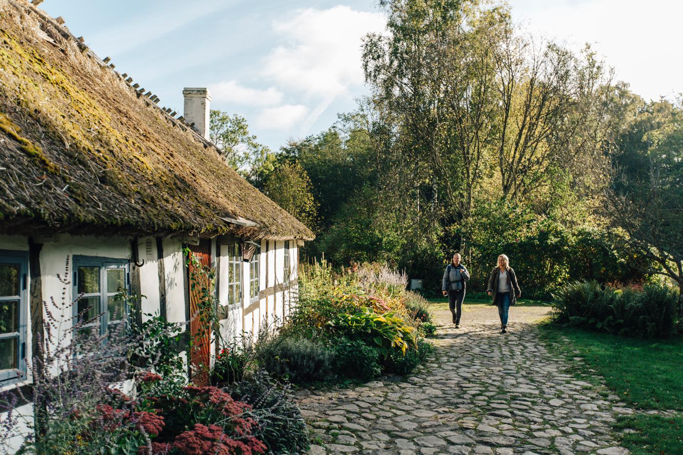 Zwei Personen mit Rucksäcken gehen neben einem weißen Kalksteinhaus.