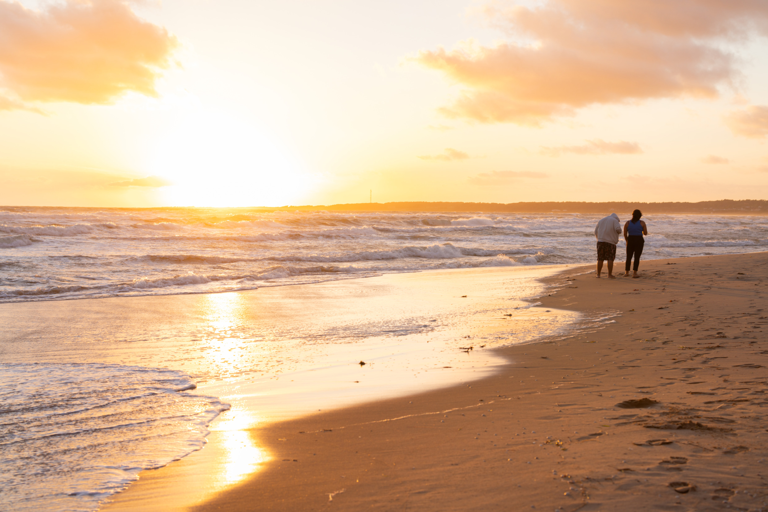 Two persons walking on the beach during the sunset.