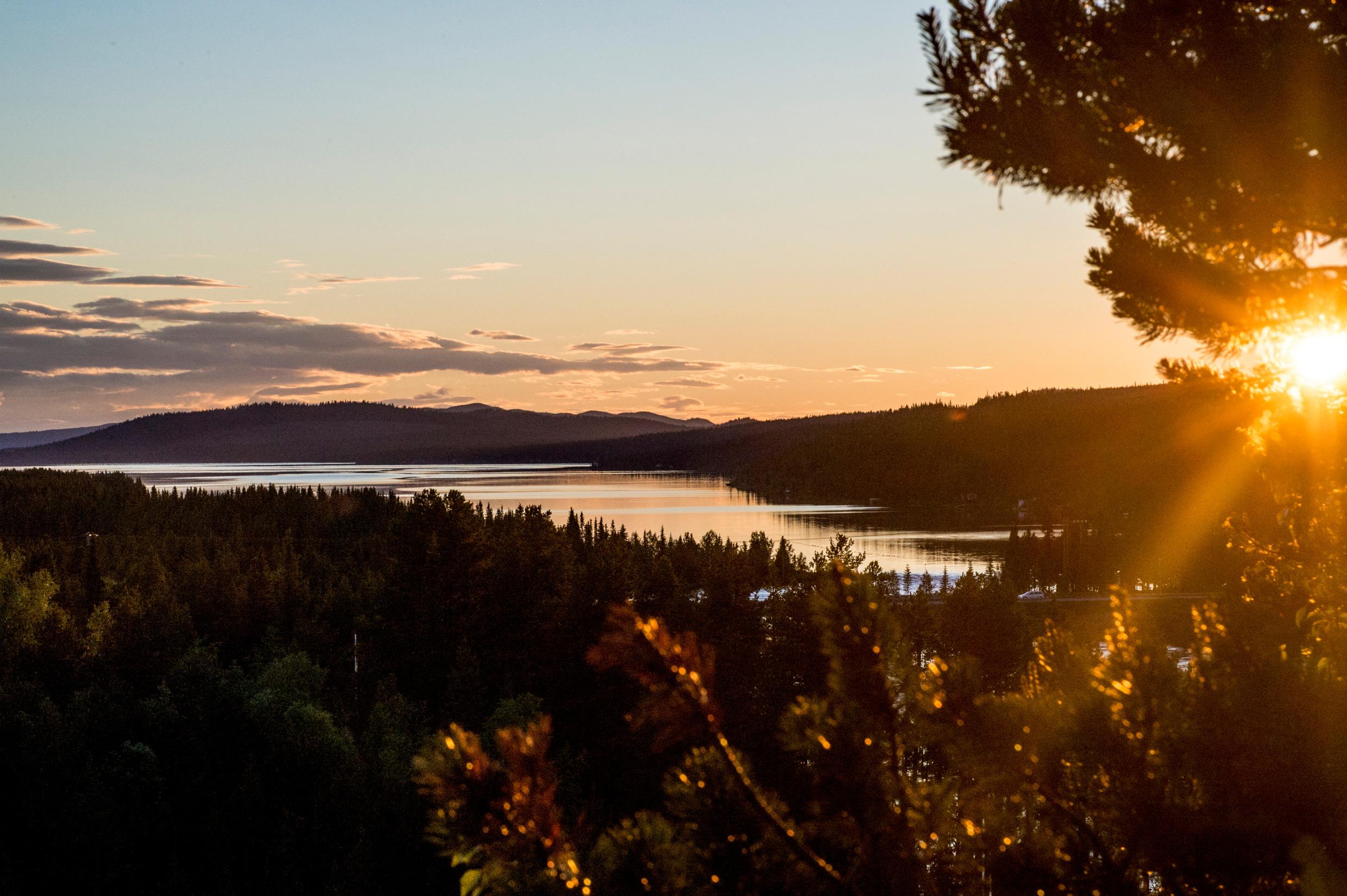 Die Mitternachtssonne über einem See und Wald in Schwedisch Lappland. Die Berge im Hintergrund.