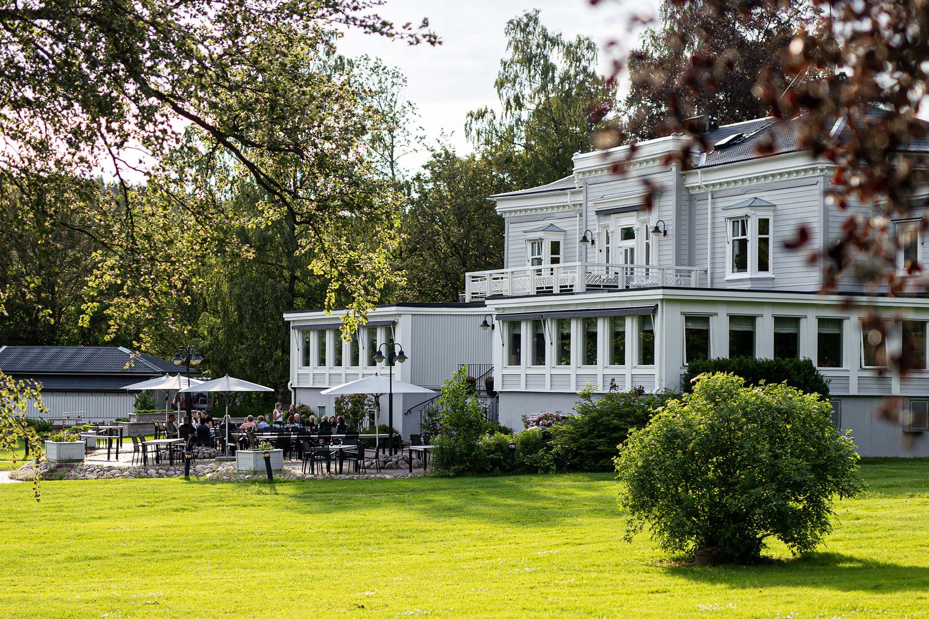 Le manoir d'Aspenäs, une demeure historique blanche entourée de jardins, dotée d'une terrasse extérieure où les convives dînent par une journée ensoleillée.