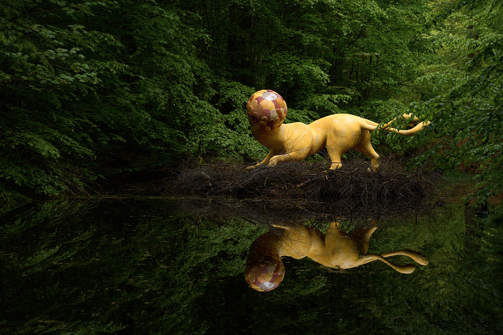 La sculpture Puruma d'Atang Tshikare, une figure jaune ressemblant à un animal avec une tête à motifs, se reflète dans l'eau du parc de sculptures Wanås Konst à Scanie, en Suède.