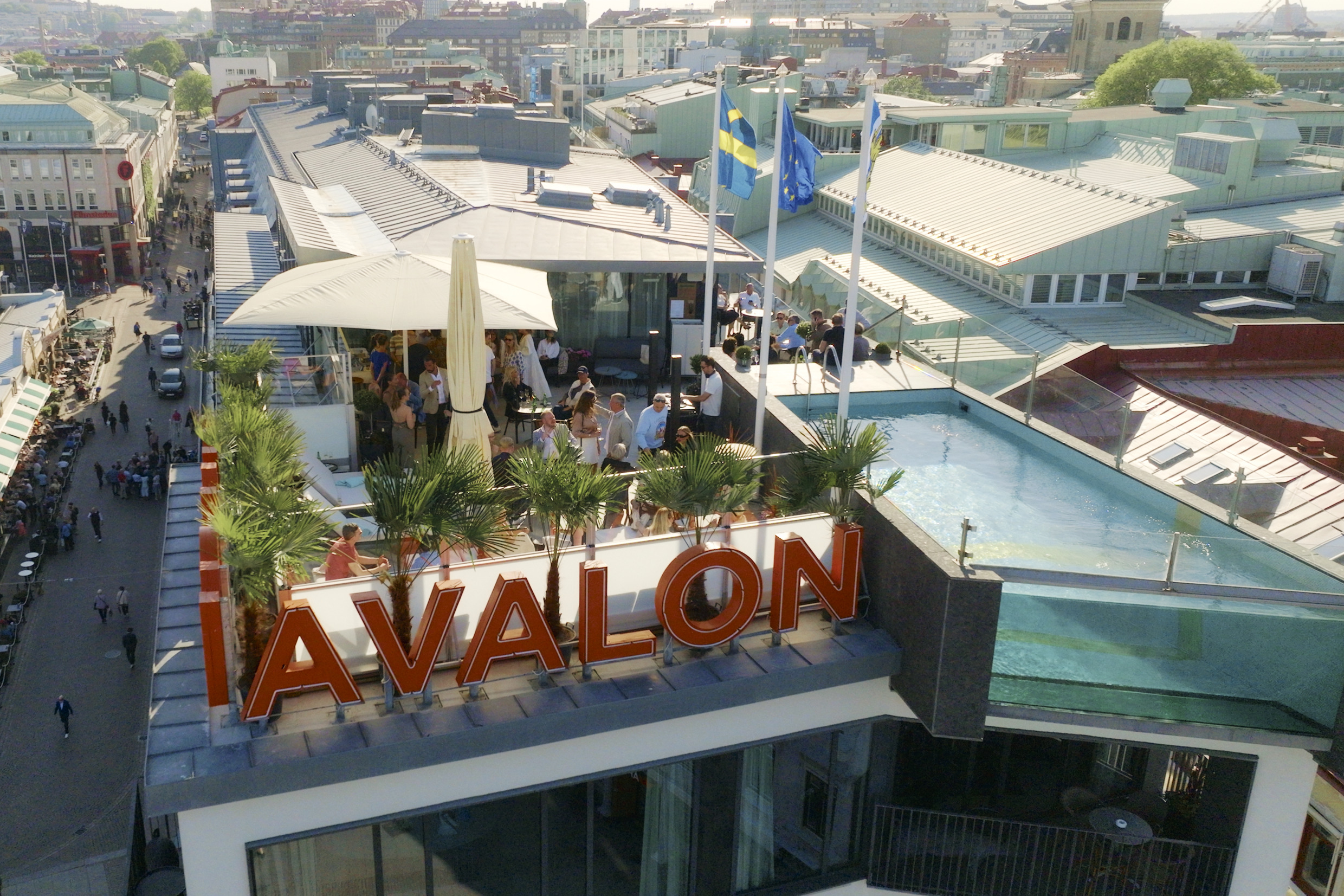 Mensen hangen rond op het dakterras van het Avalon Hotel in Göteborg, met een glazen zwembad en uitzicht over de daken van de stad.