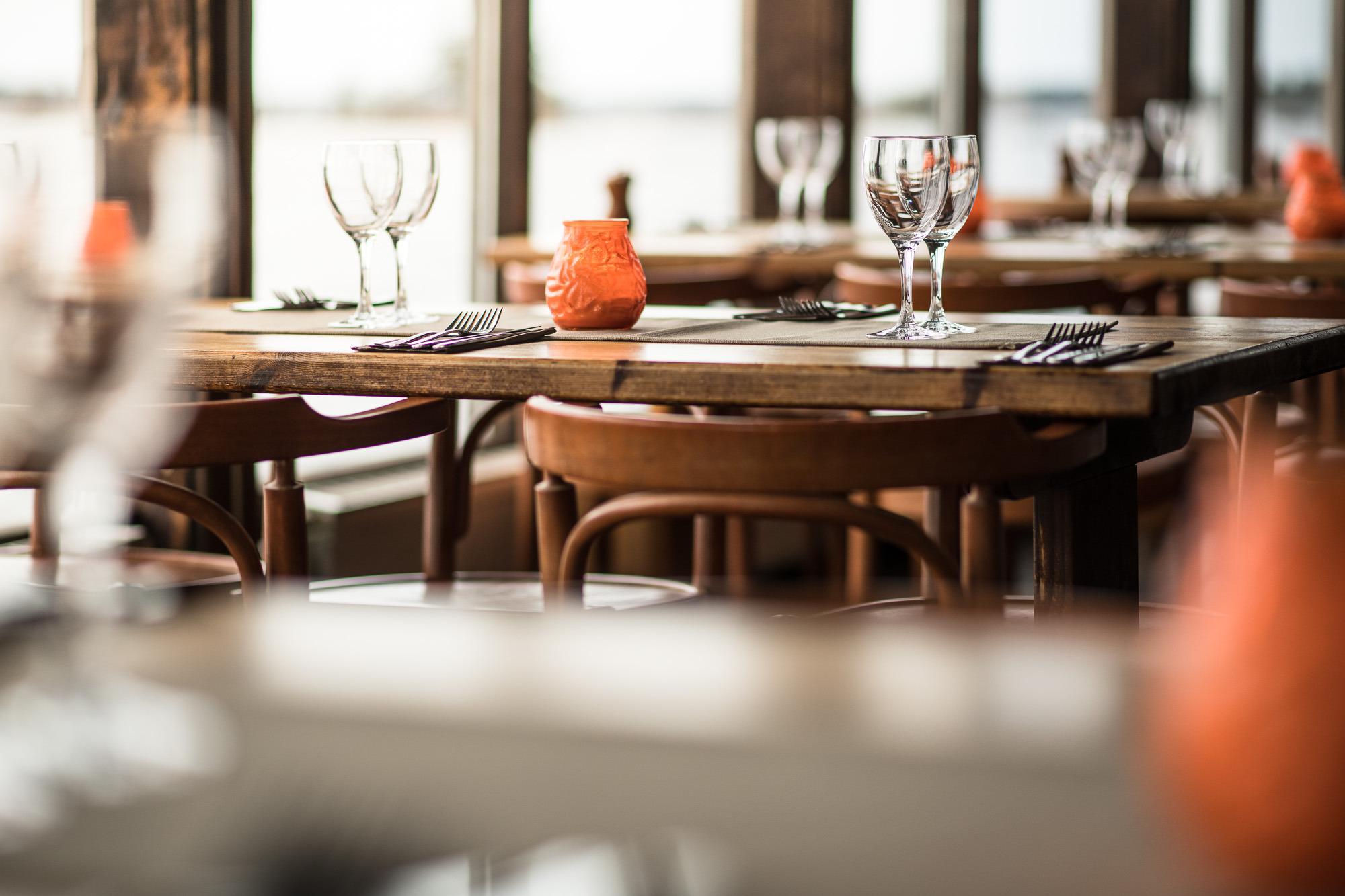 Interior from a restaurant. Close-up on wooden table set with wine glasses and orange candle lamps.