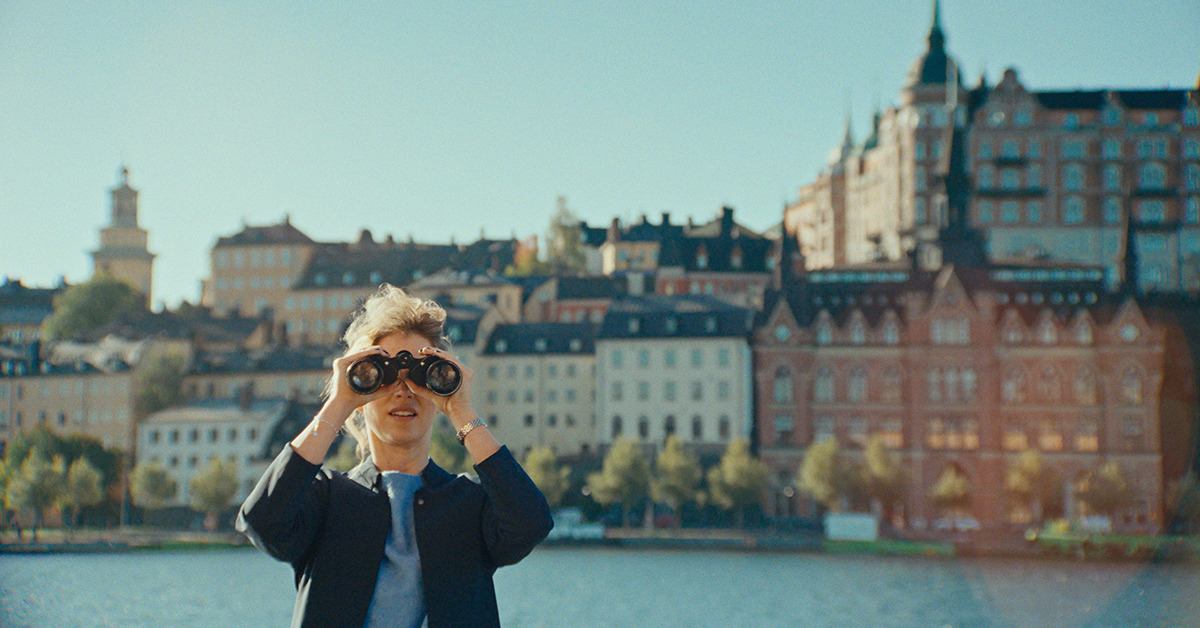 Die Schauspielerin aus dem Kampagnenvideo von Visit Sweden - Visit the Original Sweden - schaut durch ein Fernglas. Im Hintergrund sind Gebäude der Stadt Stockholm zu sehen.