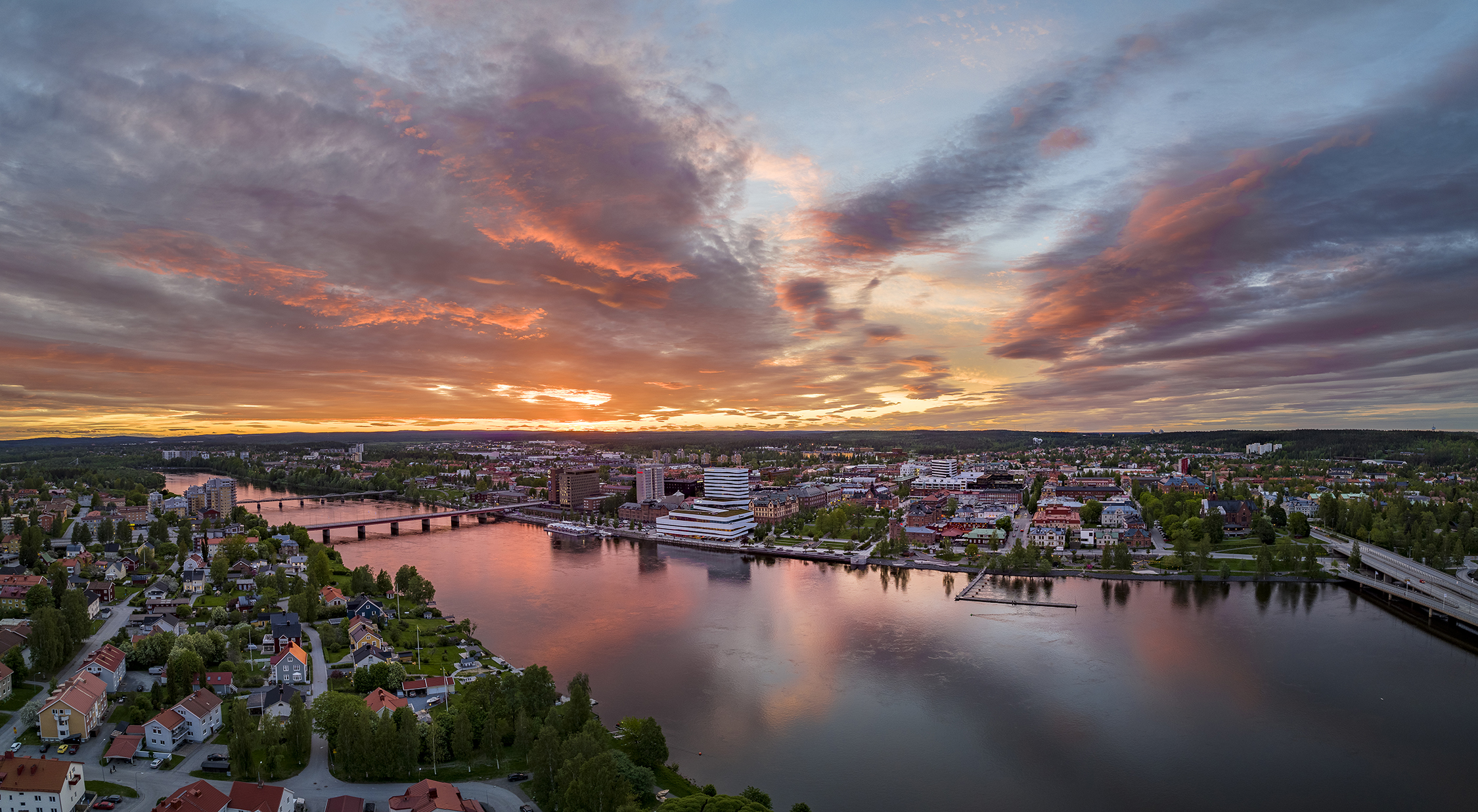 Aerial view of central Umeå at sunset, with the Ume River flowing through the city under a colourful summer sky.