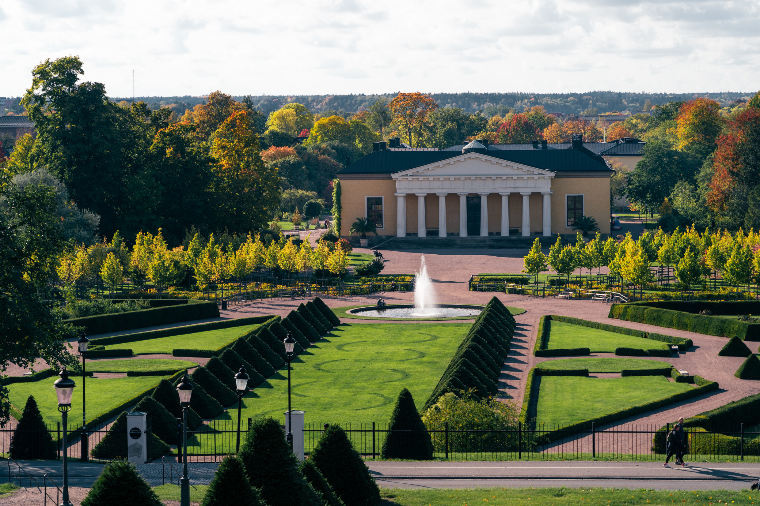 Botanische tuin in Uppsala. Herfst met gekleurde bladeren gemengd met groen. Uitzicht over de barokke tuin. Op de achtergrond het gebouw Linneanum.