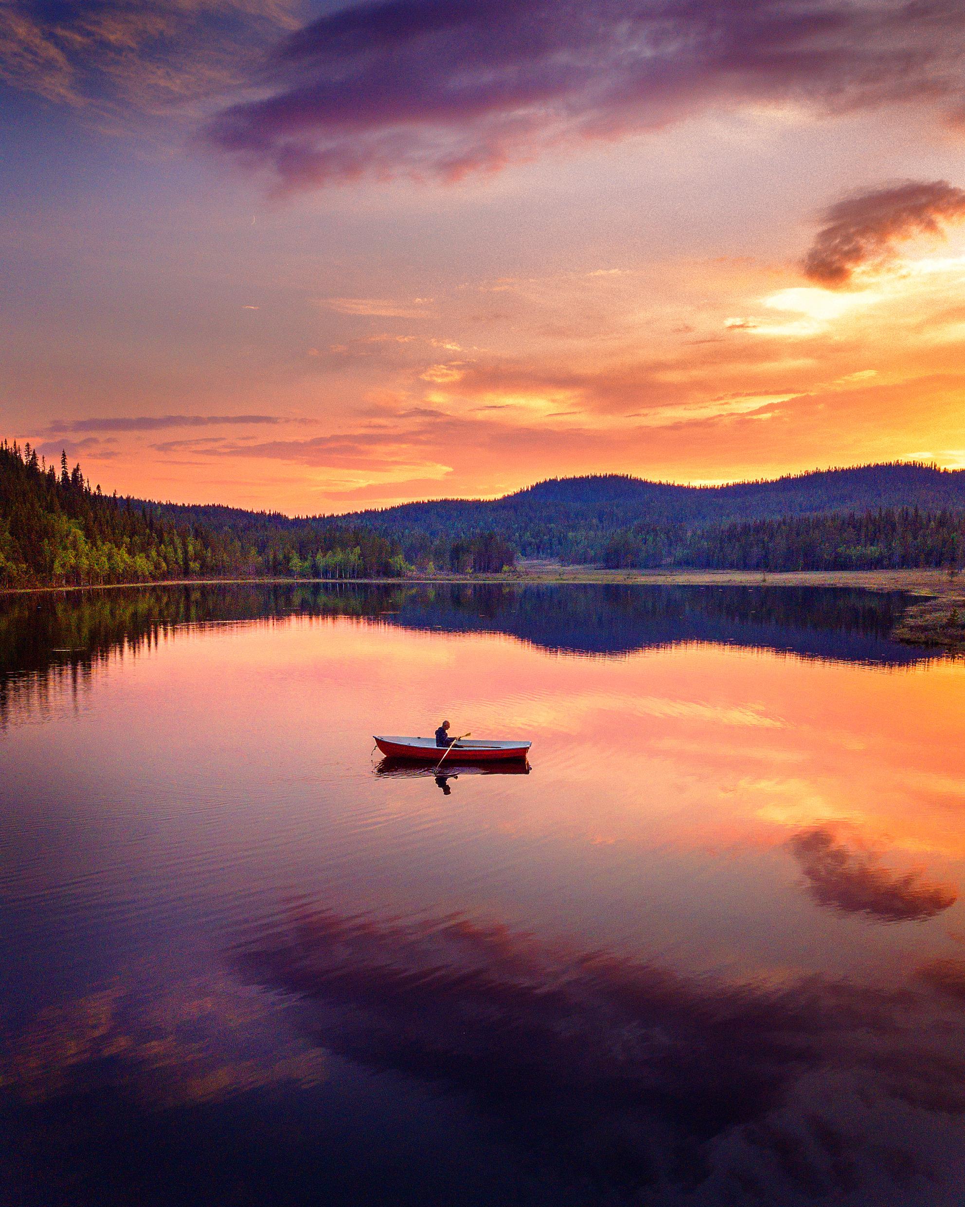 A person is rowing a boat on a mirrored lake under the midnight sun in Swedish Lapland.