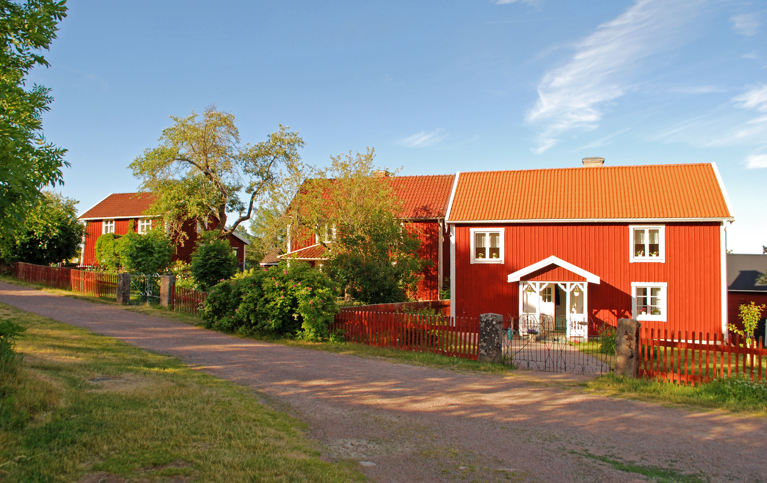Three red houses with white corners and a large garden on a summer day.