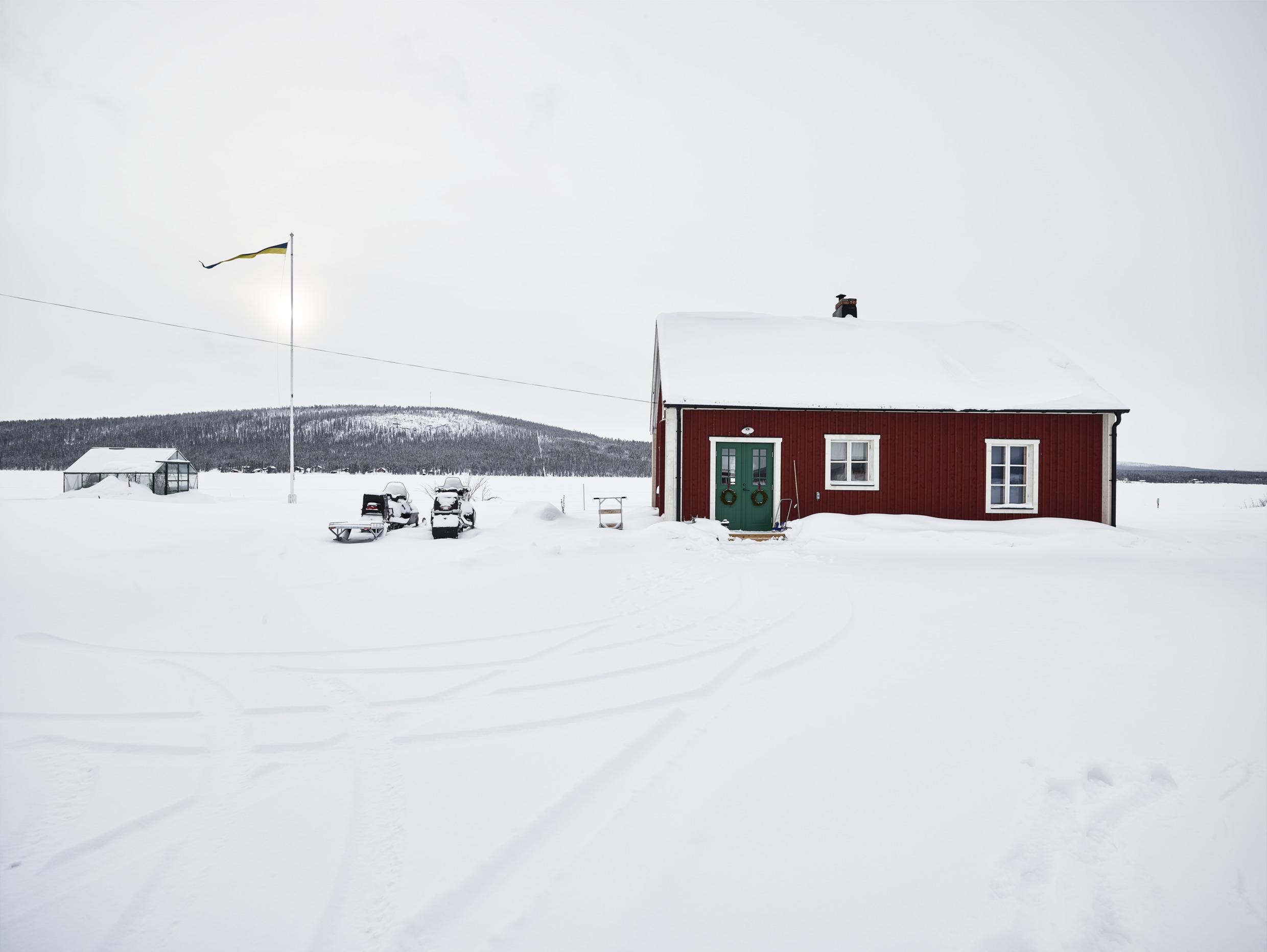 Une maison rouge à côté d'une serre enneigée avec des motoneiges garées à l'extérieur.