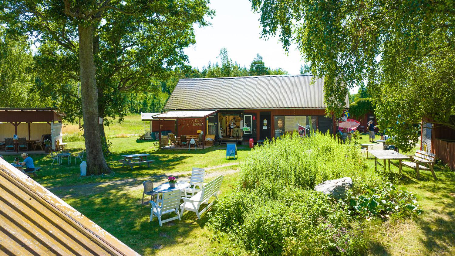 Een café in een rood houten huis omgeven door groen tijdens een zomerse dag.