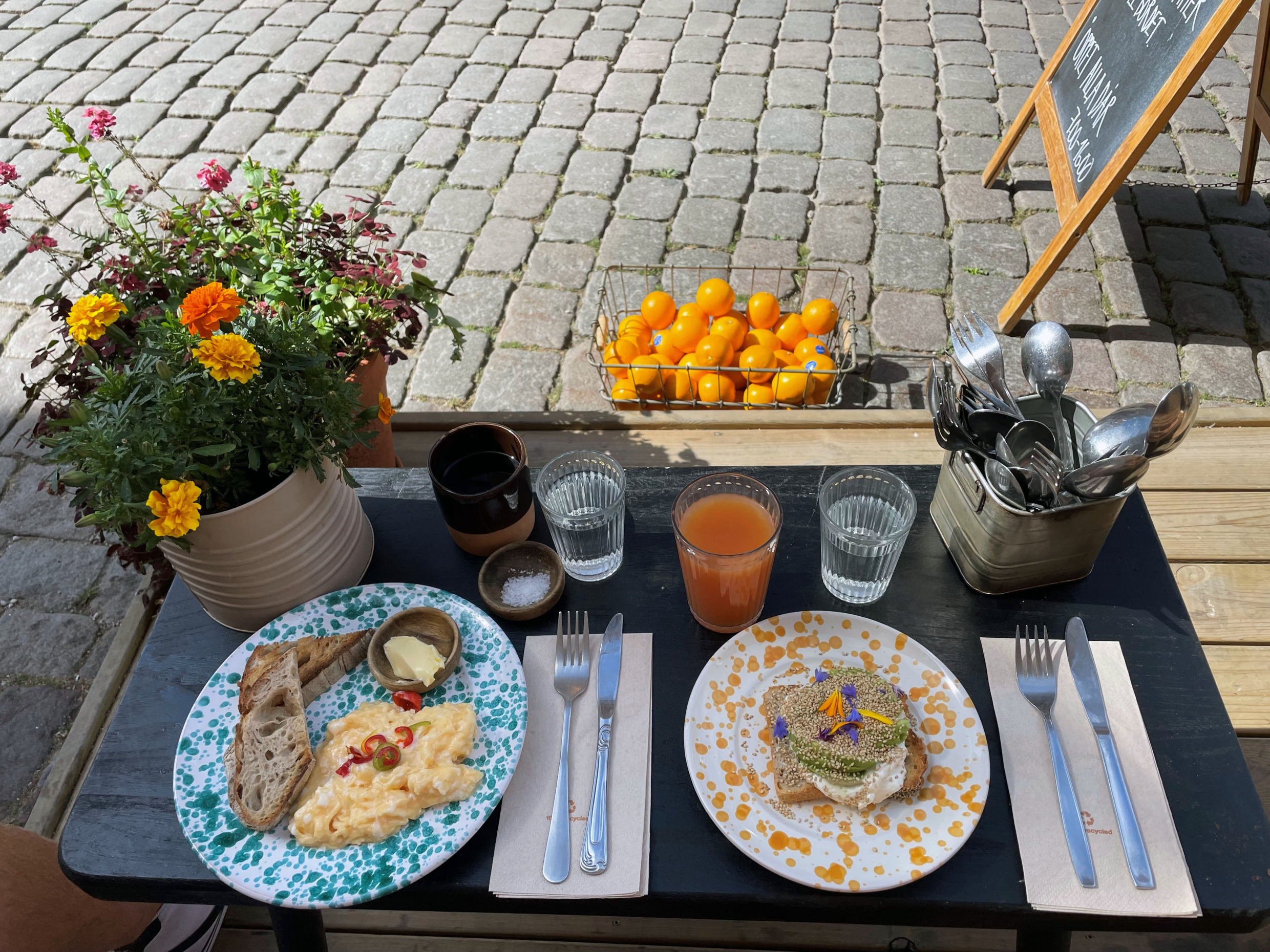 Outdoor breakfast with eggs, toast and juice at Café Amalia in Visby, set against cobblestones and fresh flowers.
