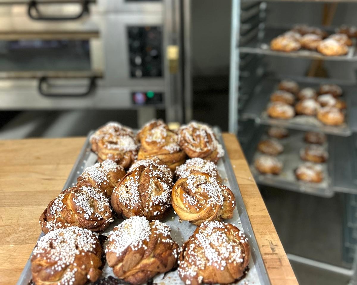 Tray of freshly baked cinnamon buns topped with pearl sugar in a café kitchen.
