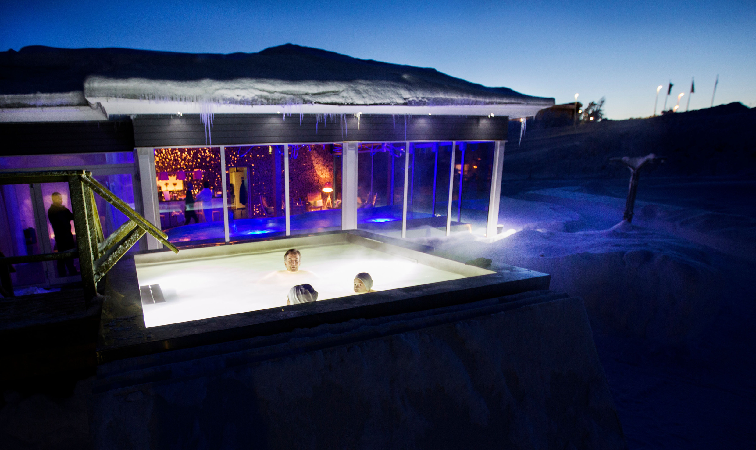 Drie mensen baden in een buitenzwembad tijdens de winter.