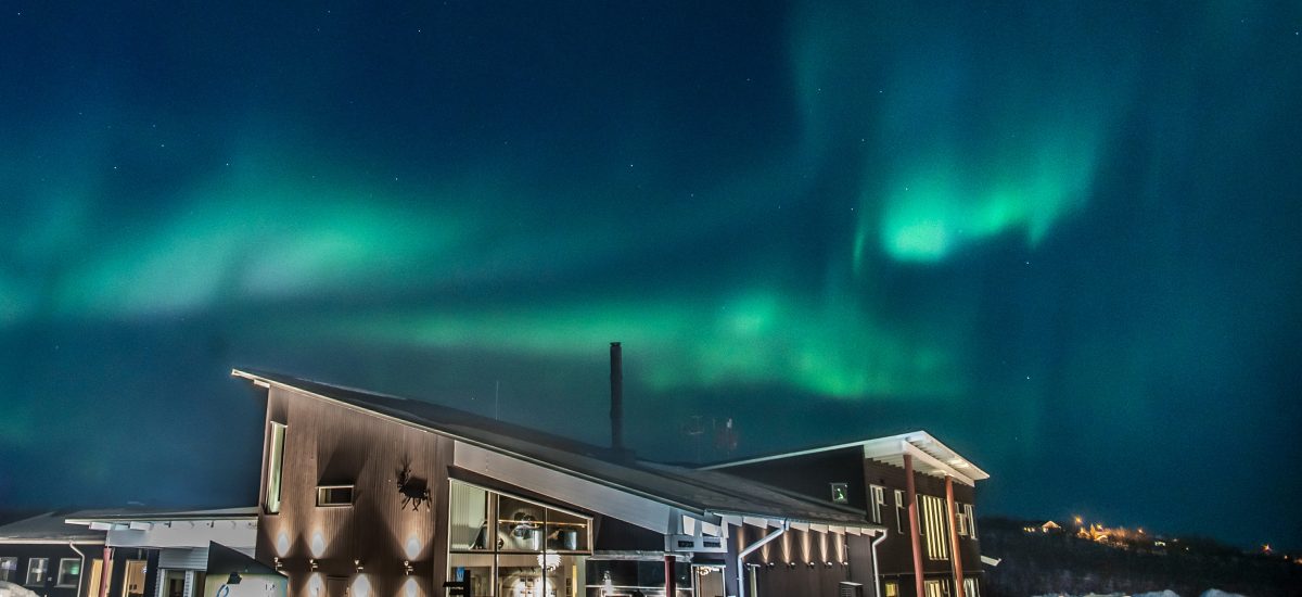 The Northern Lights glowing green across the night sky above Camp Ripan in snow-covered Kiruna.