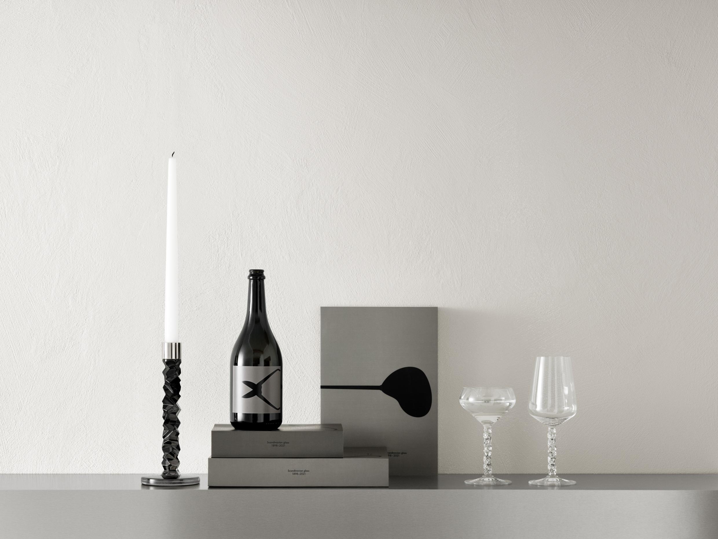 Un chandelier noir avec une bougie blanche, trois livres et deux verres posés sur une table.