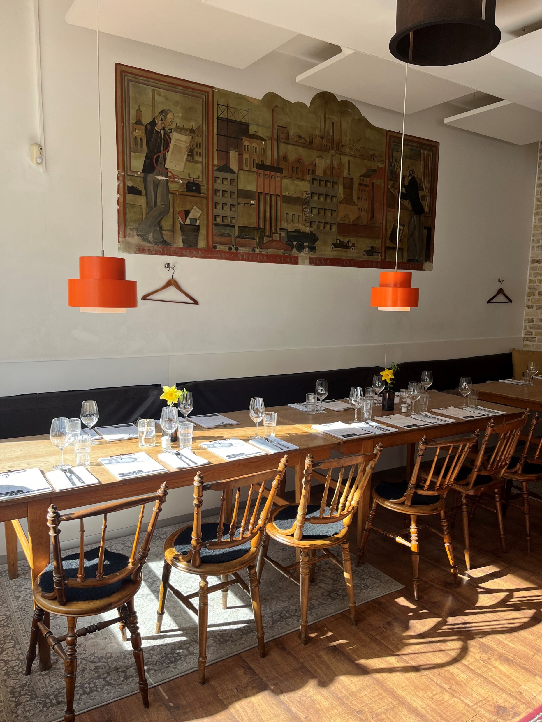 Long wooden dining table with vintage chairs and a mural at Château Forêt restaurant in Helsingborg.