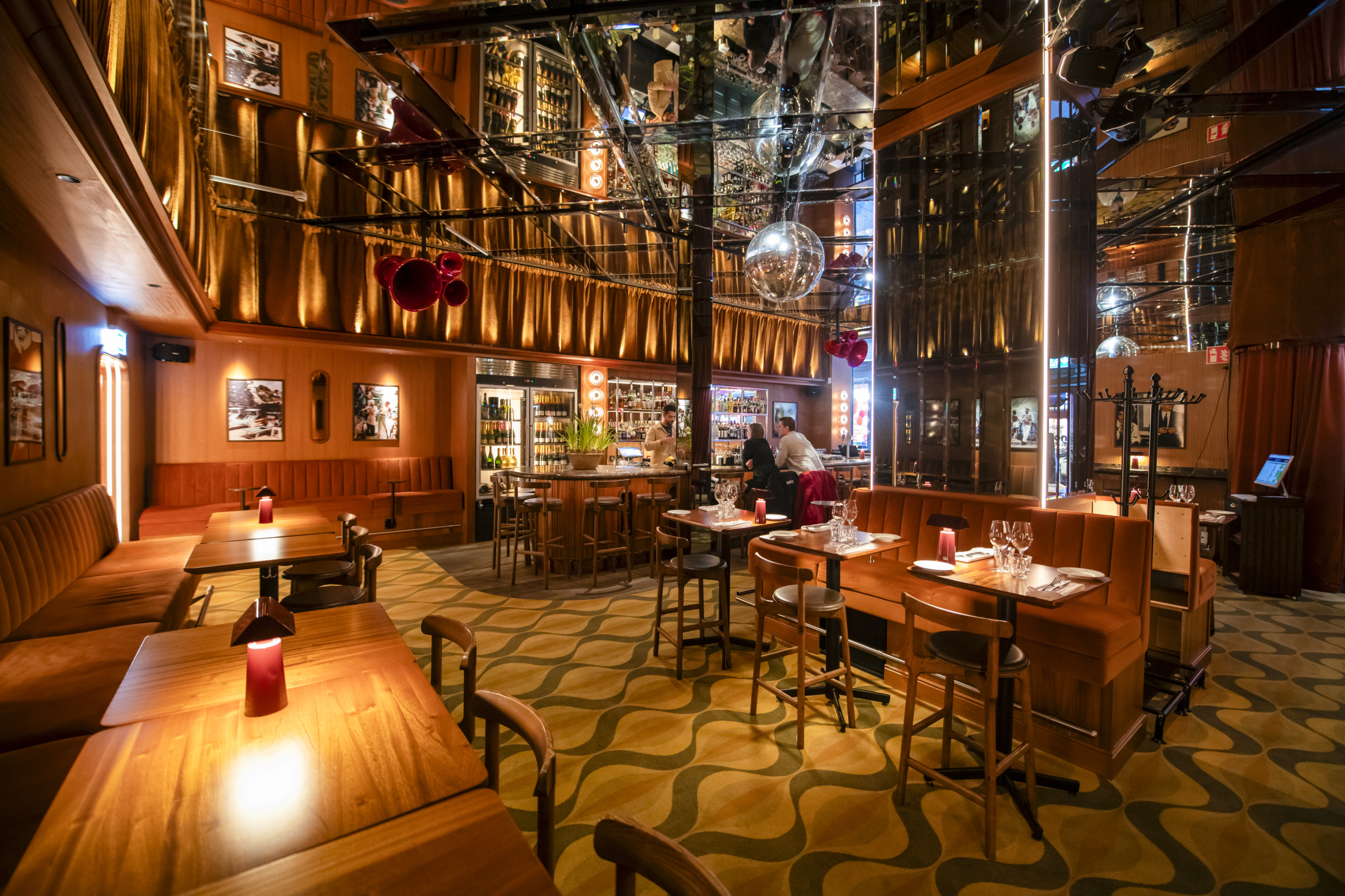 Intérieur du restaurant Collage à Göteborg, avec un éclairage chaleureux, des plafonds à miroirs, des sièges confortables et un bar d'inspiration rétro.