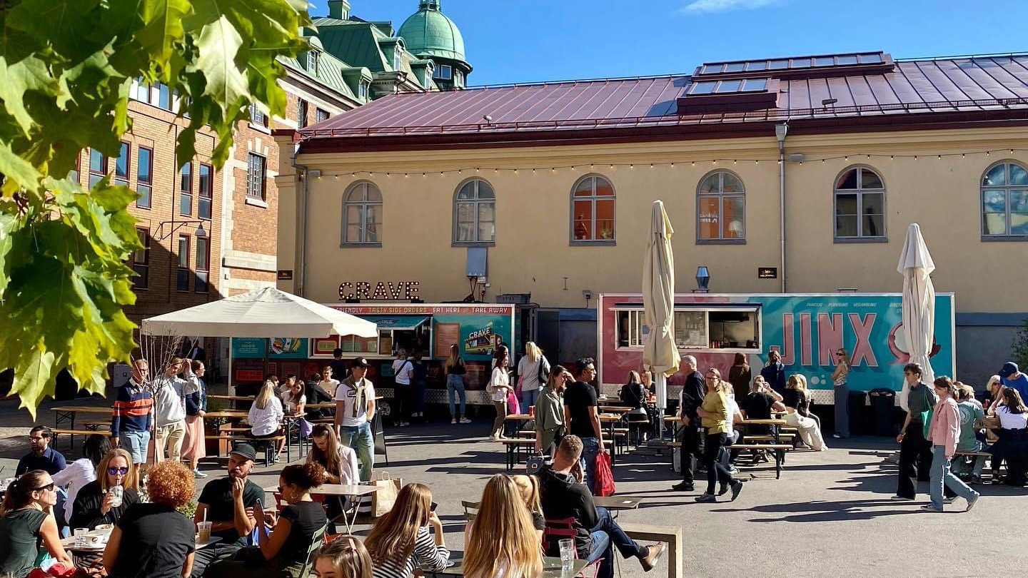 Des personnes assises à des tables de pique-nique devant deux food-trucks pendant une journée d'été.